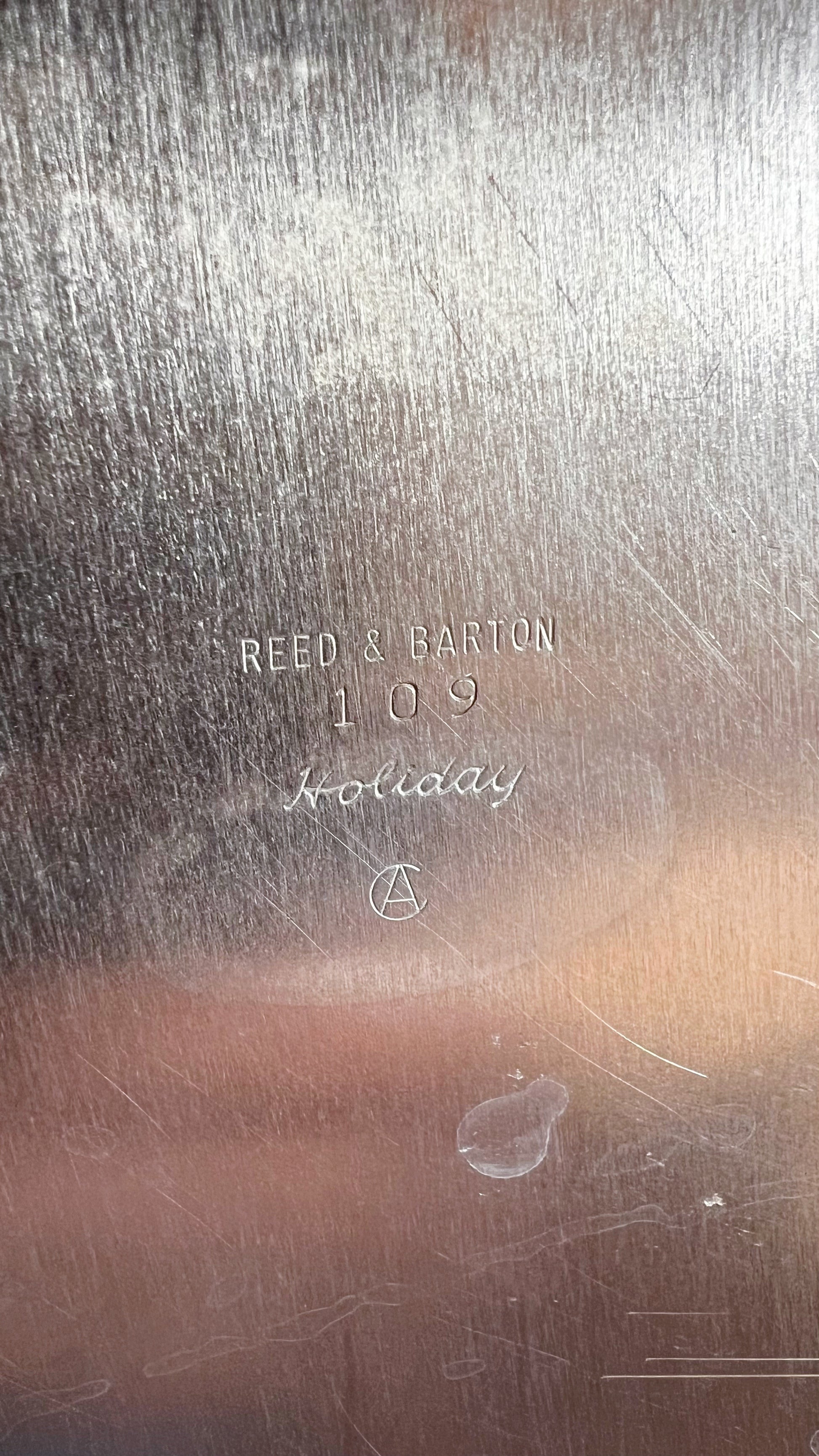 Close-up of a silver surface with engraved text reading 'REED & BARTON 109 Holiday' and a small circular logo.