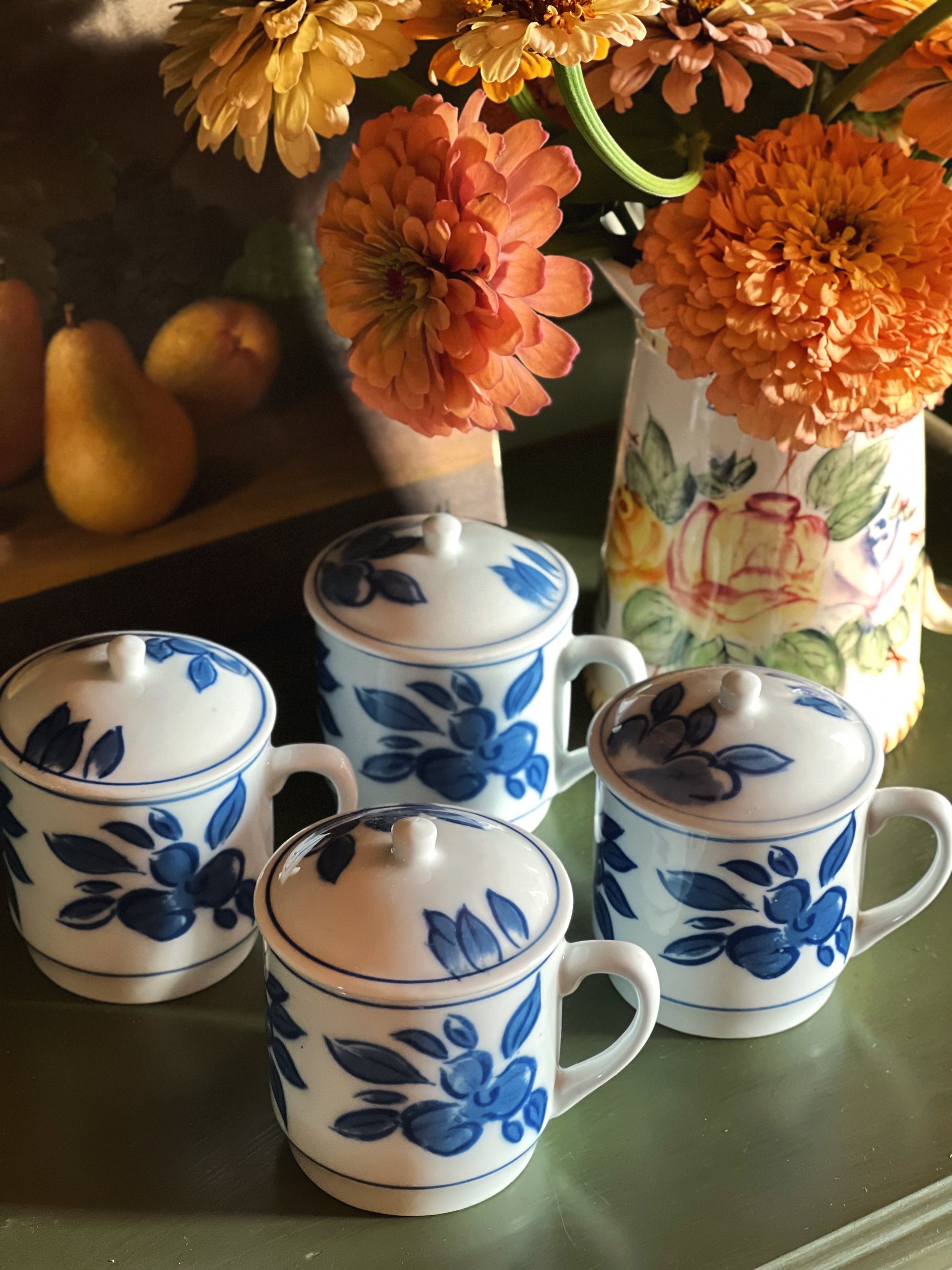Vintage blue and white porcelain lidded mugs with floral pattern arranged together beside autumn flowers.