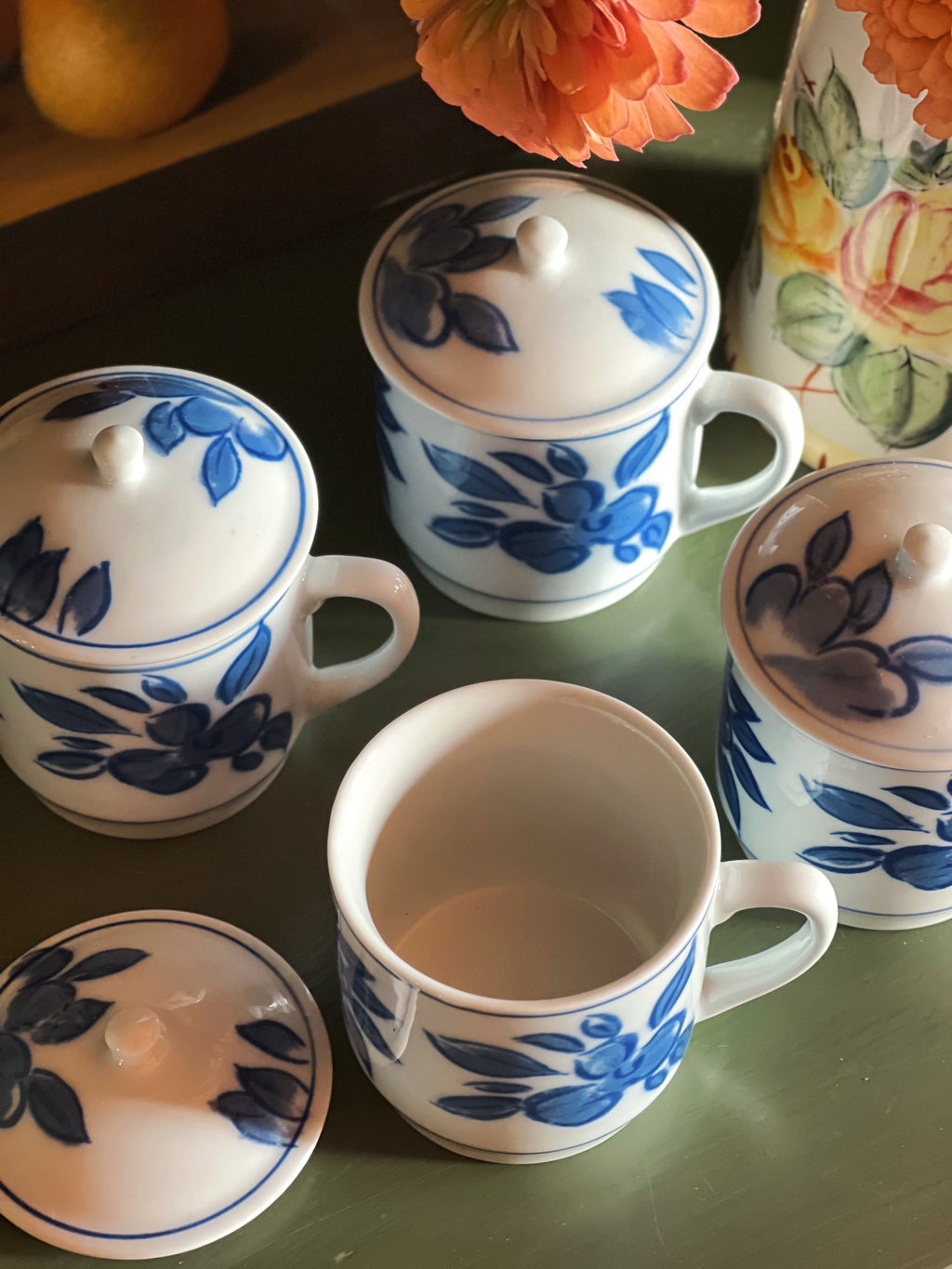 Vintage blue and white porcelain lidded mugs with floral pattern arranged together beside autumn flowers.