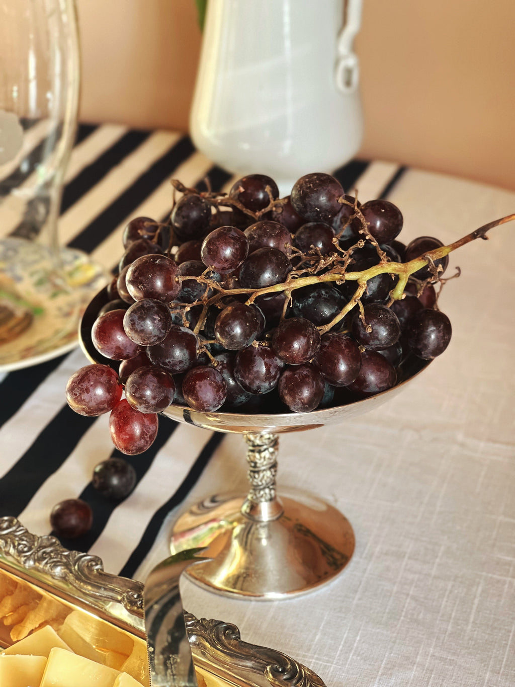 Vintage Valero Spain Silver Compote Coupe filled with grapes on a table set with a striped tablecloth