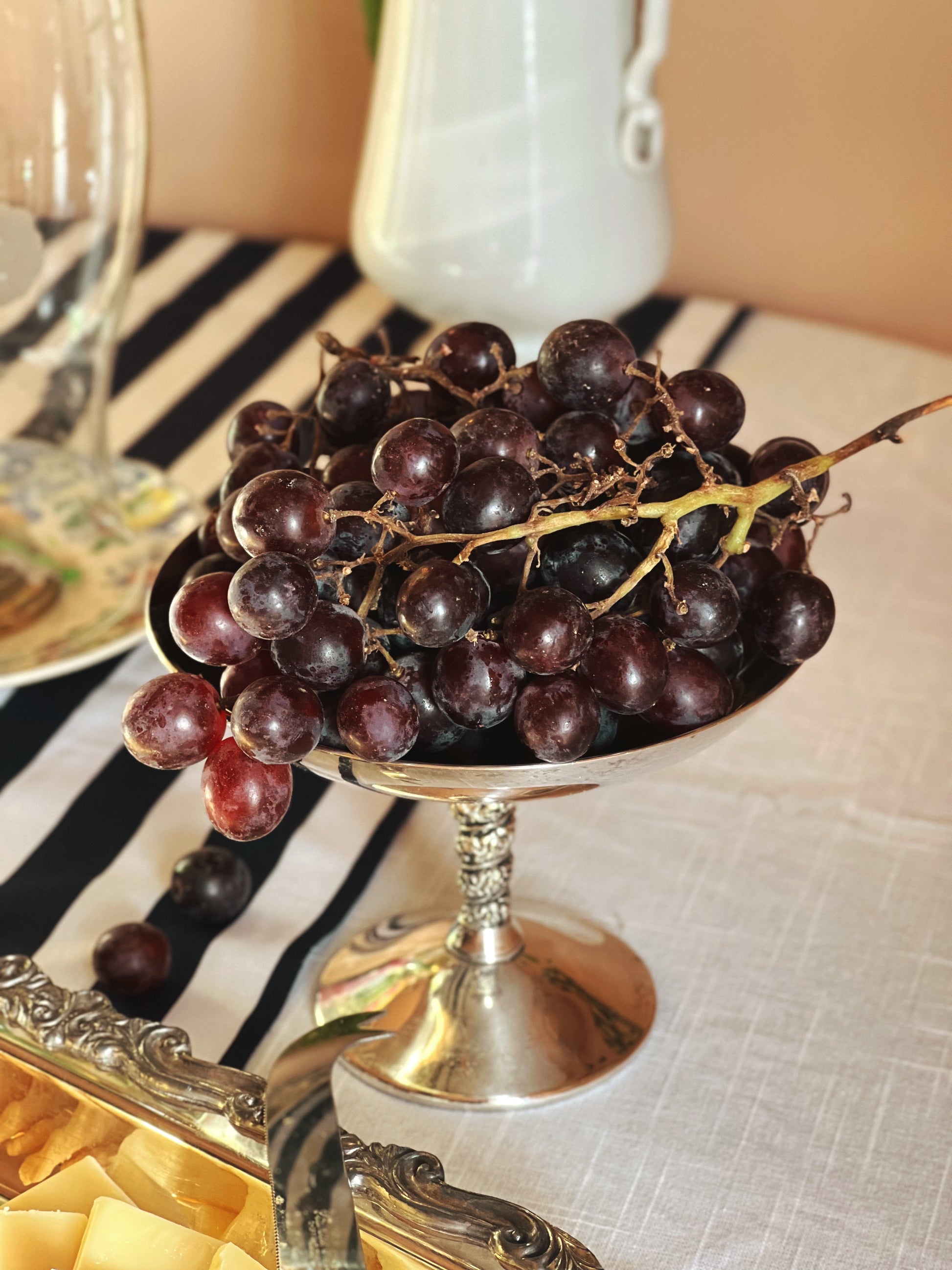 Vintage Valero Spain Silver Compote Coupe filled with grapes on a table set with a striped tablecloth