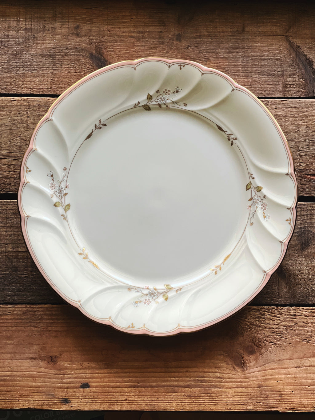 Vintage Mikasa Monticello dinner plate made in Japan with a delicate blush floral border and gold trim on a rustic wood surface.