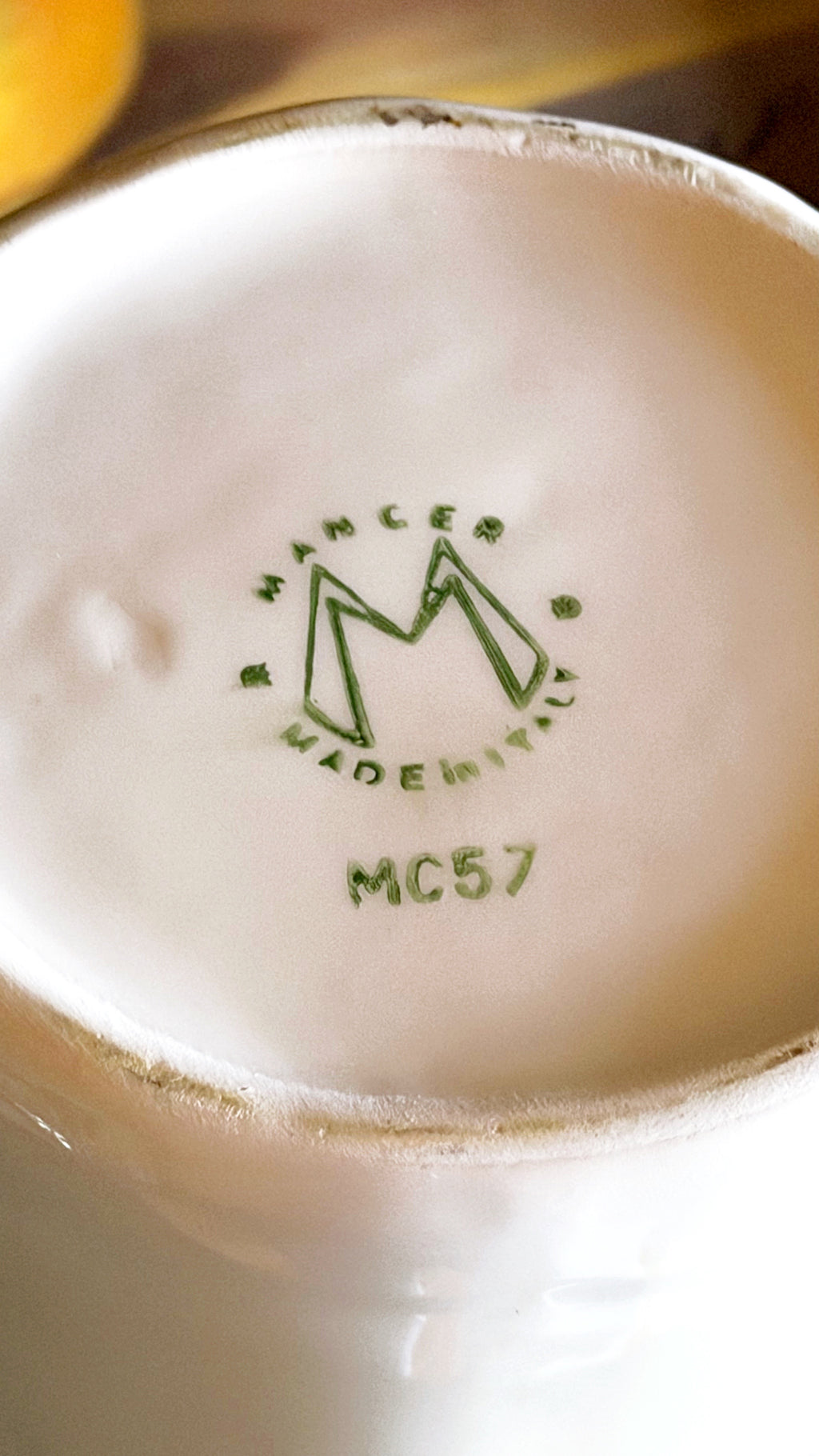 Close-up of the bottom of a white ceramic cup or mug showing a green Mancer Made in Italy stamp with model MC57.