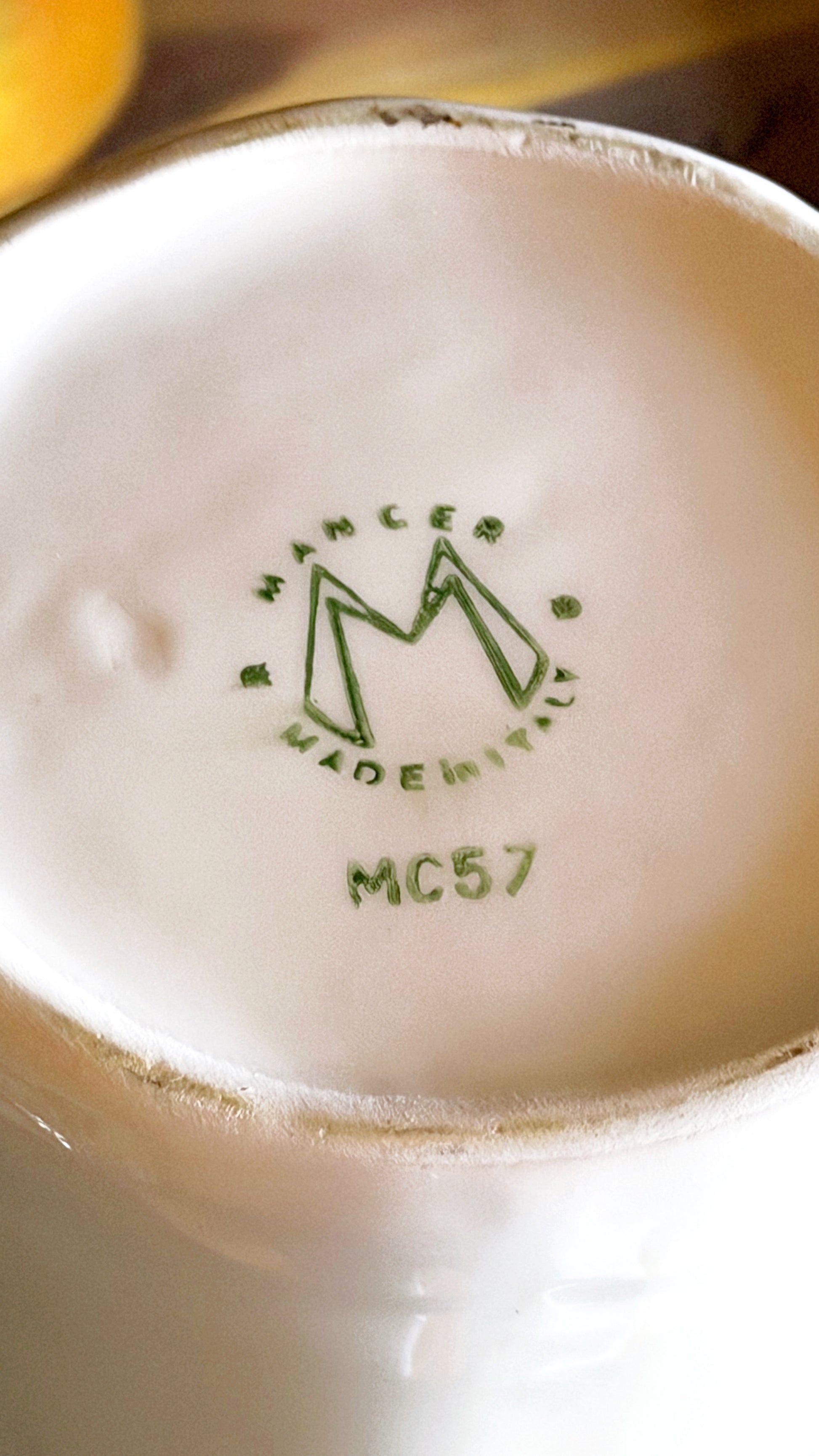 Close-up of the bottom of a white ceramic cup or mug showing a green Mancer Made in Italy stamp with model MC57.