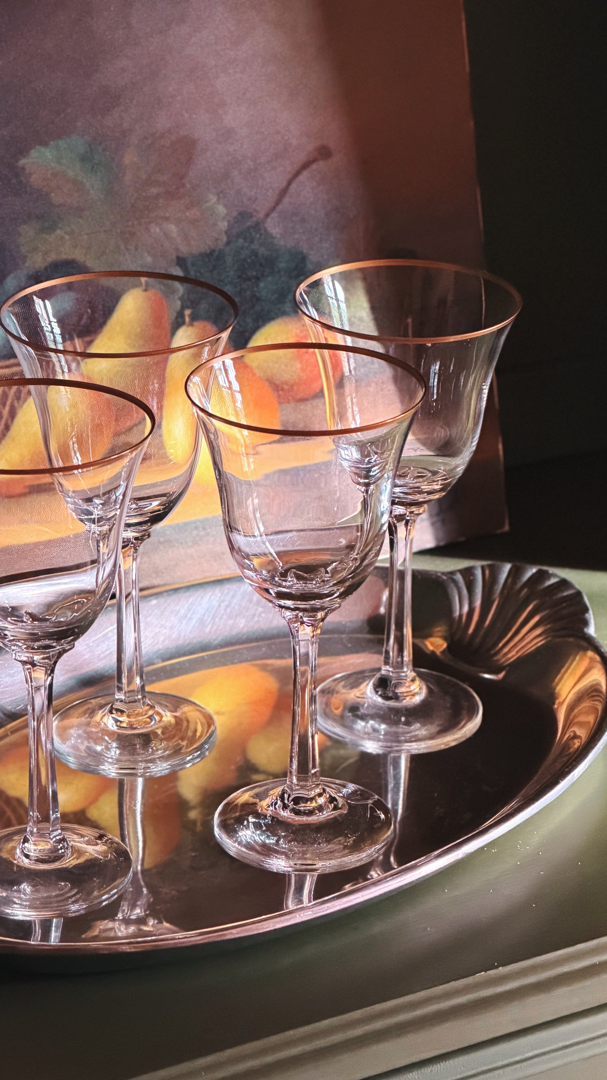 Four Vintage Lenox Hayworth Crystal Wine Glass with Gold Rims arranged on a reflective silver tray, with a warm-toned abstract painting in the background.