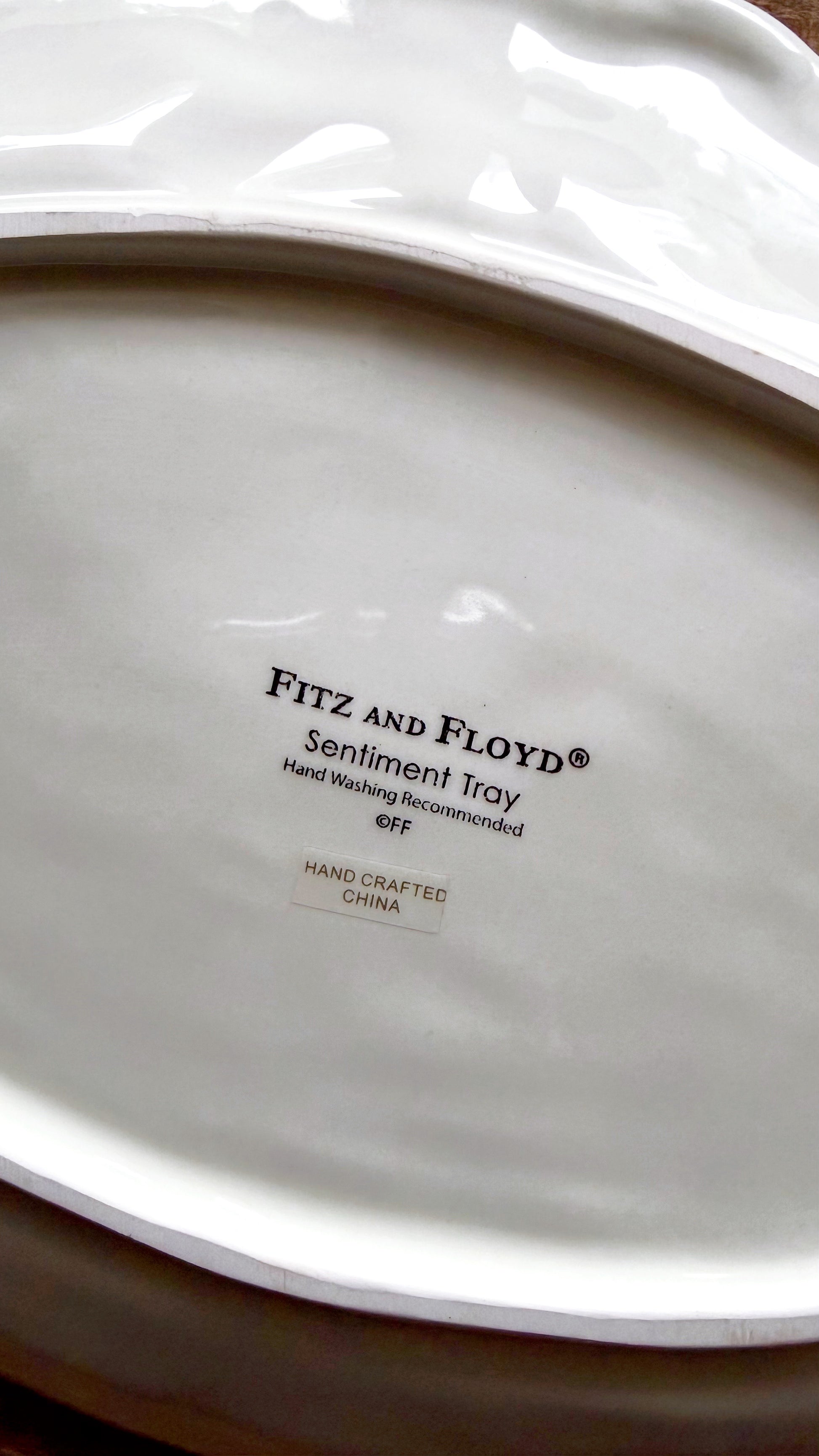 Close-up of the inside of a white ceramic plate or tray, showing the printed text 'FITZ AND FLOYD Sentiment Tray' and 'HAND CRAFTED IN CHINA'.