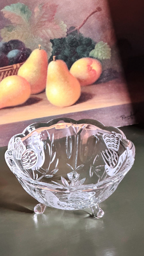 Vintage Crystal Footed Bowl with Etched Bird Design, placed on a dark surface in front of a still life painting of pears.