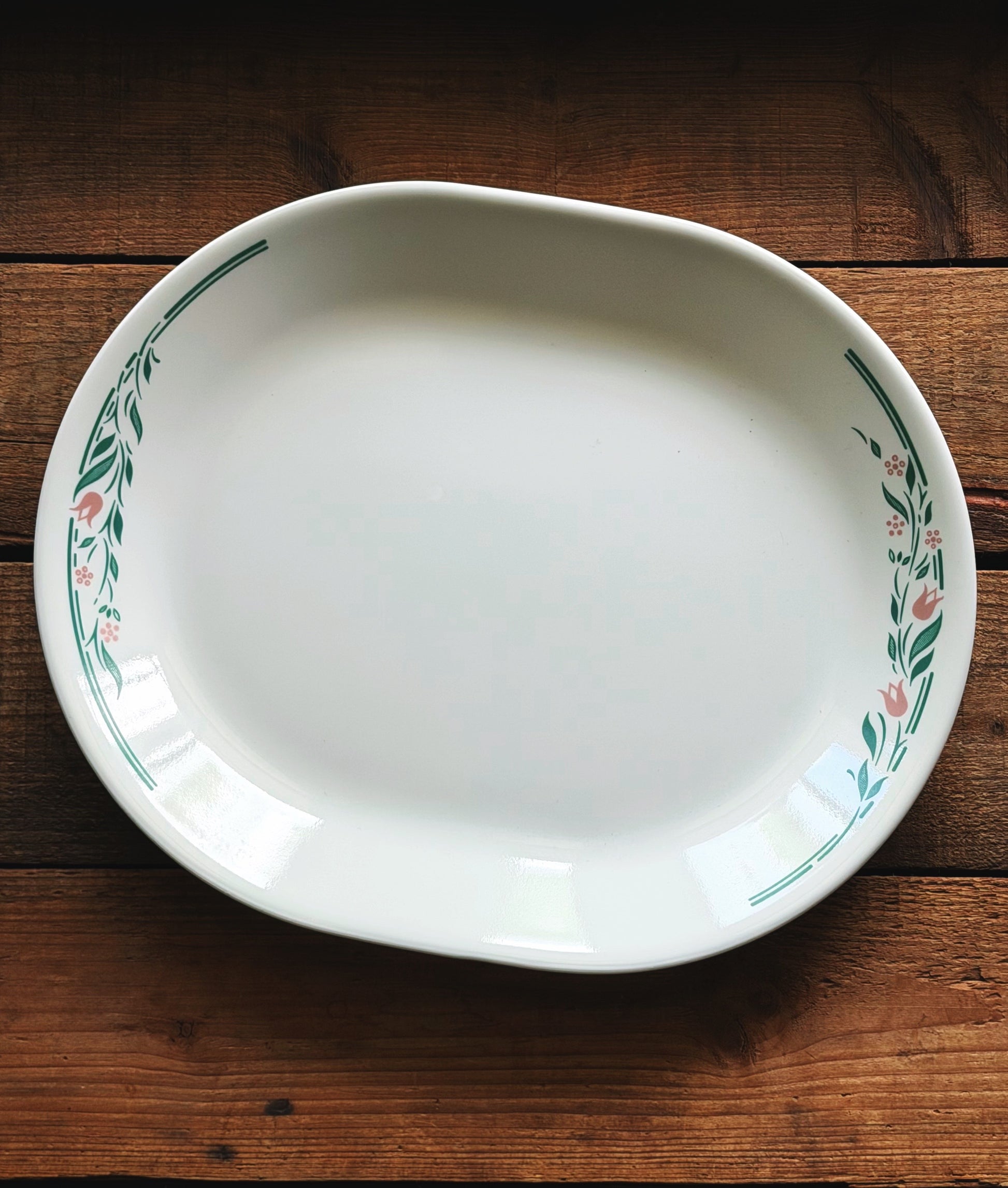 A white ceramic oval serving platter with a green floral border pattern, photographed from above on a rustic dark wood background.
