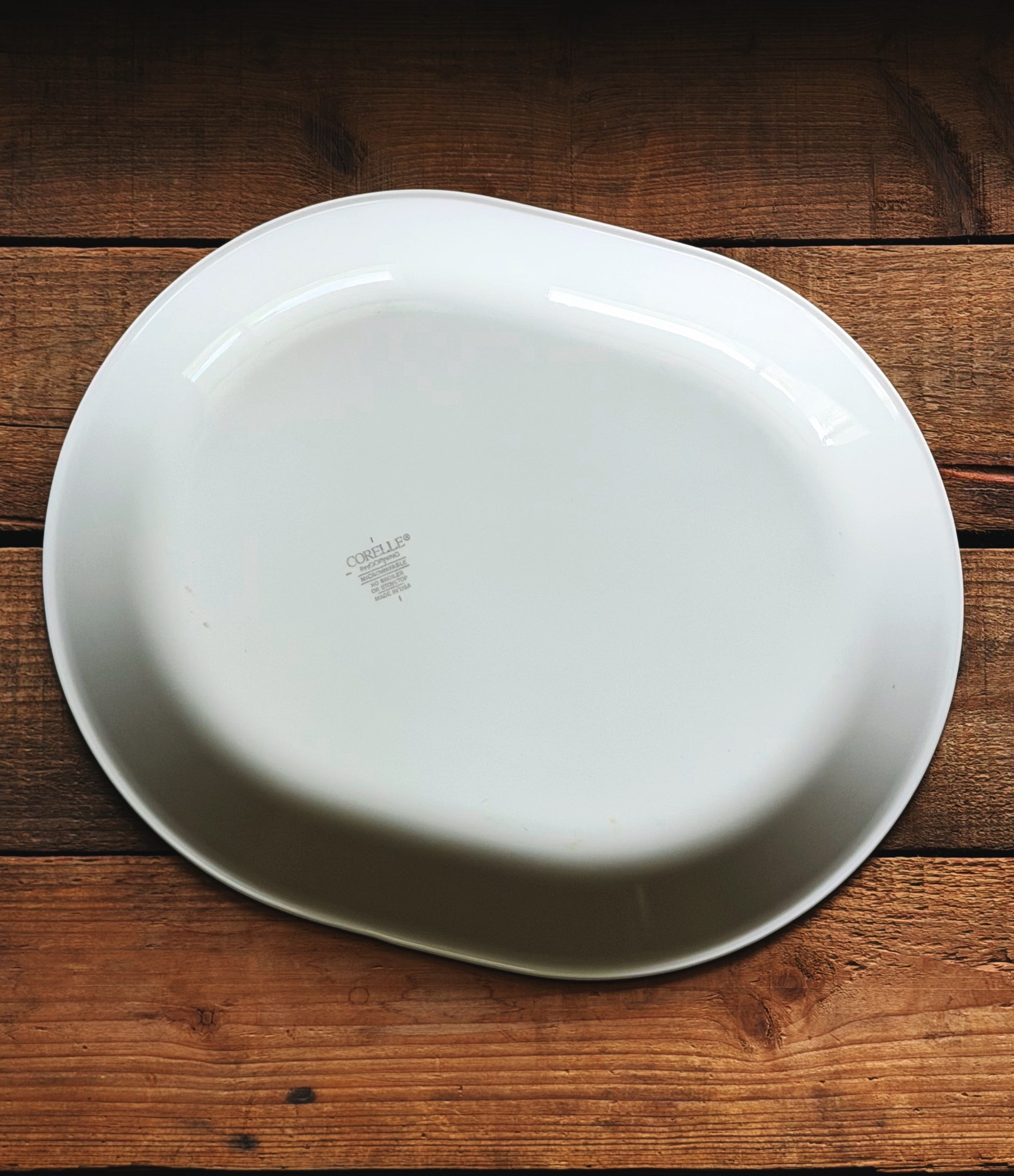 Underside of a Vintage Corelle Rosemarie Oval Serving Platter, photographed from directly above on a rustic dark brown wooden plank surface.