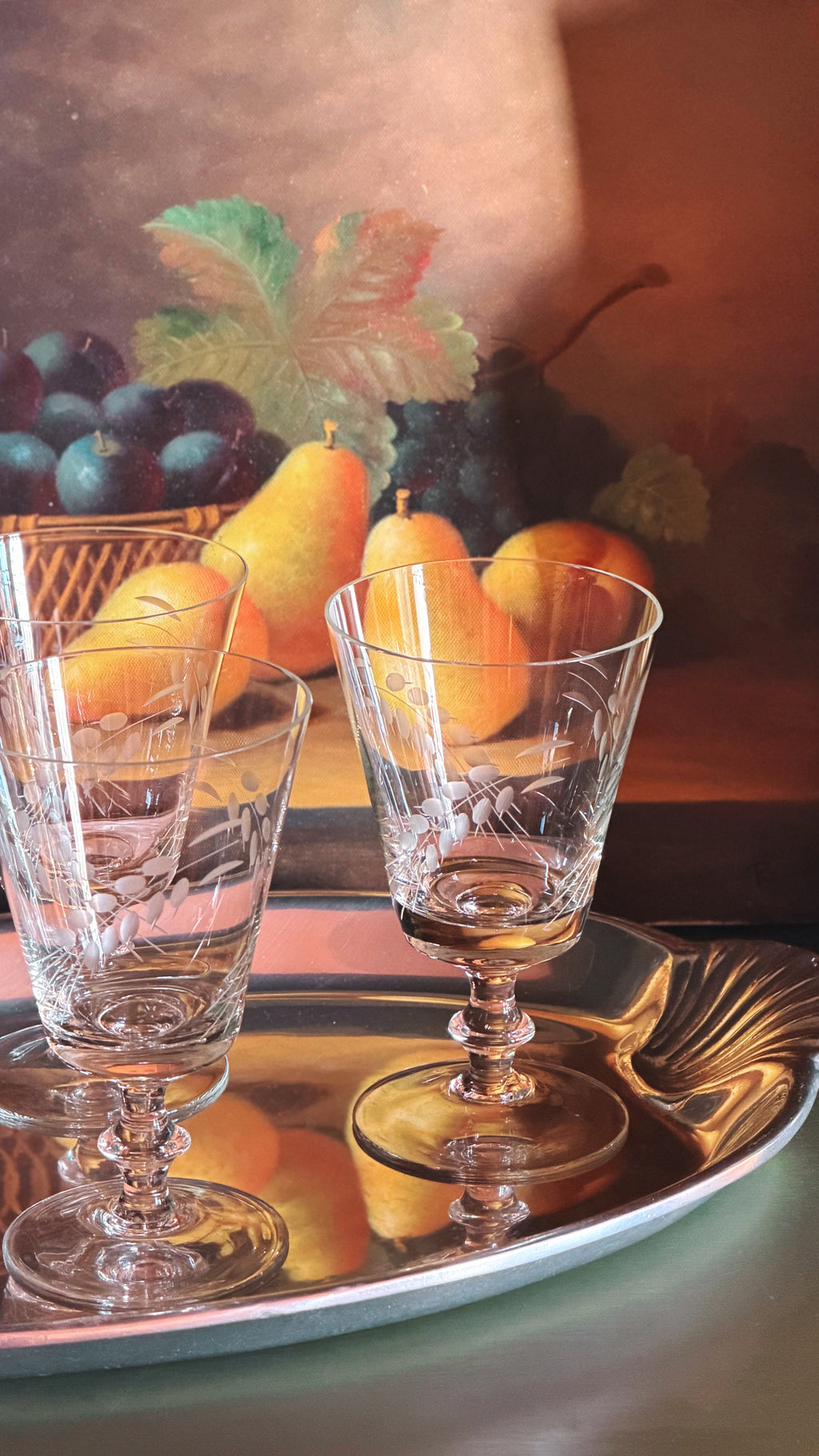 Set of 4 Vintage Etched Wine Glasses with Wheat Sheaf Design on a reflective silver tray, set against a warm-toned still life painting of pears, grapes, and a leaf.