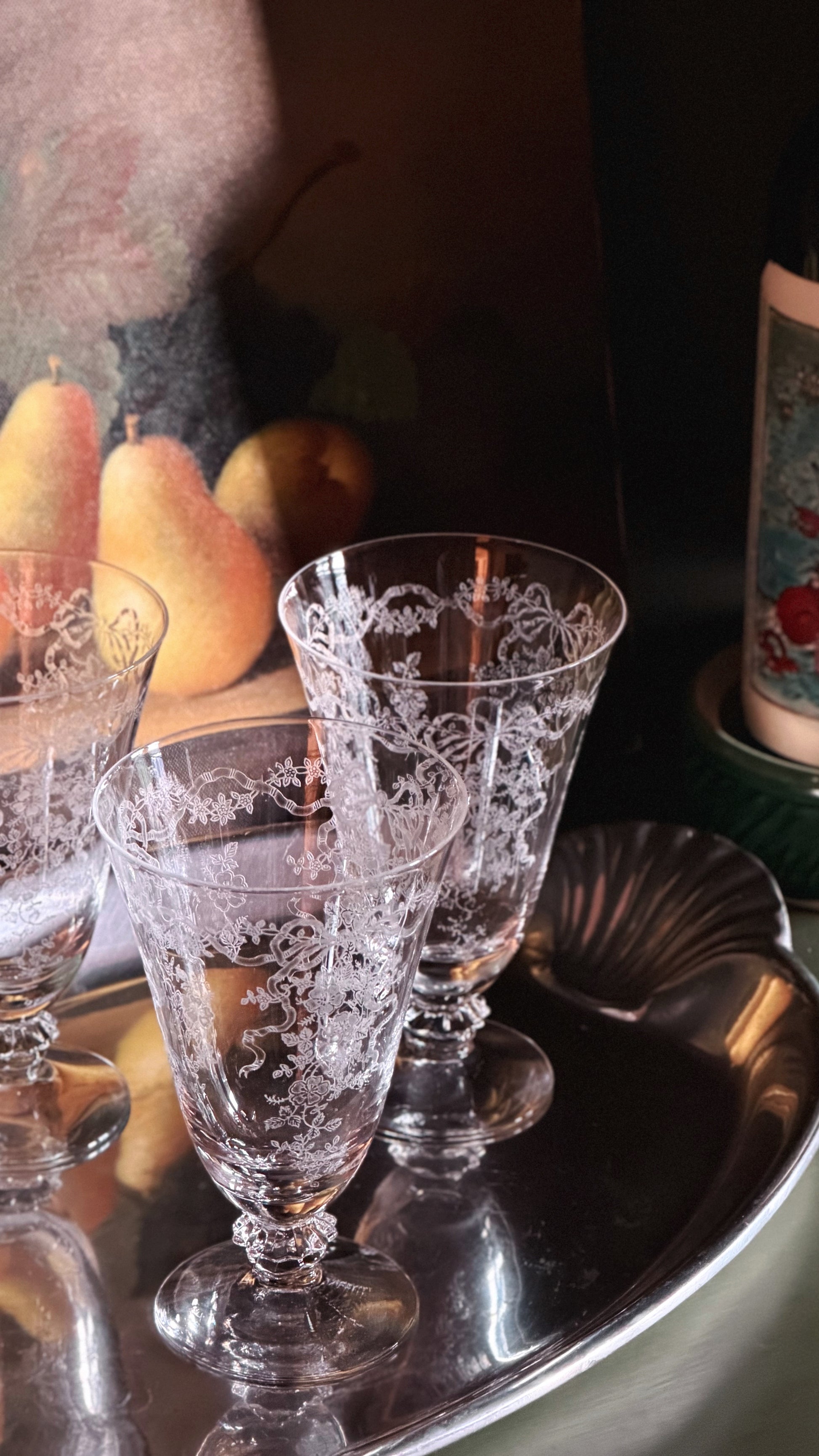 Three clear crystal wine glasses with etched floral patterns, arranged on a silver tray with a dark background.