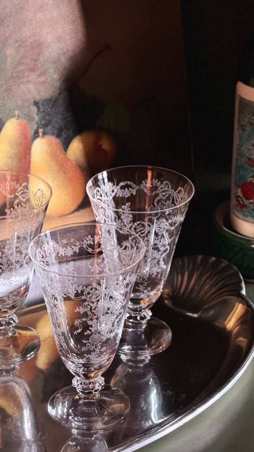 Three clear crystal wine glasses with etched floral patterns, arranged on a silver tray with a dark background.