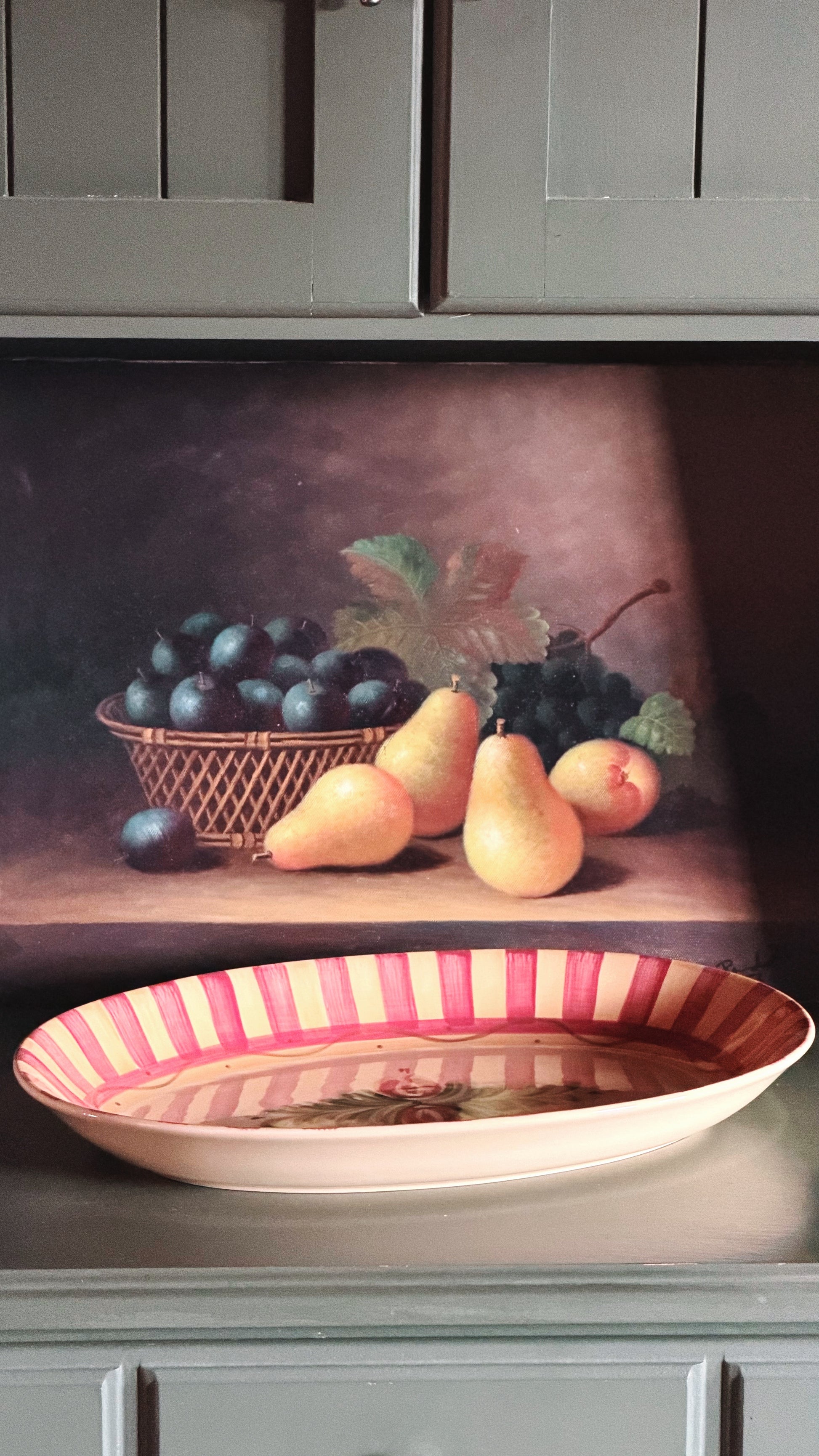 A Vintage Gail Pittman Siena Serving Platter sits on a kitchen counter in front of a painted still life wall mural showing grapes and pears.