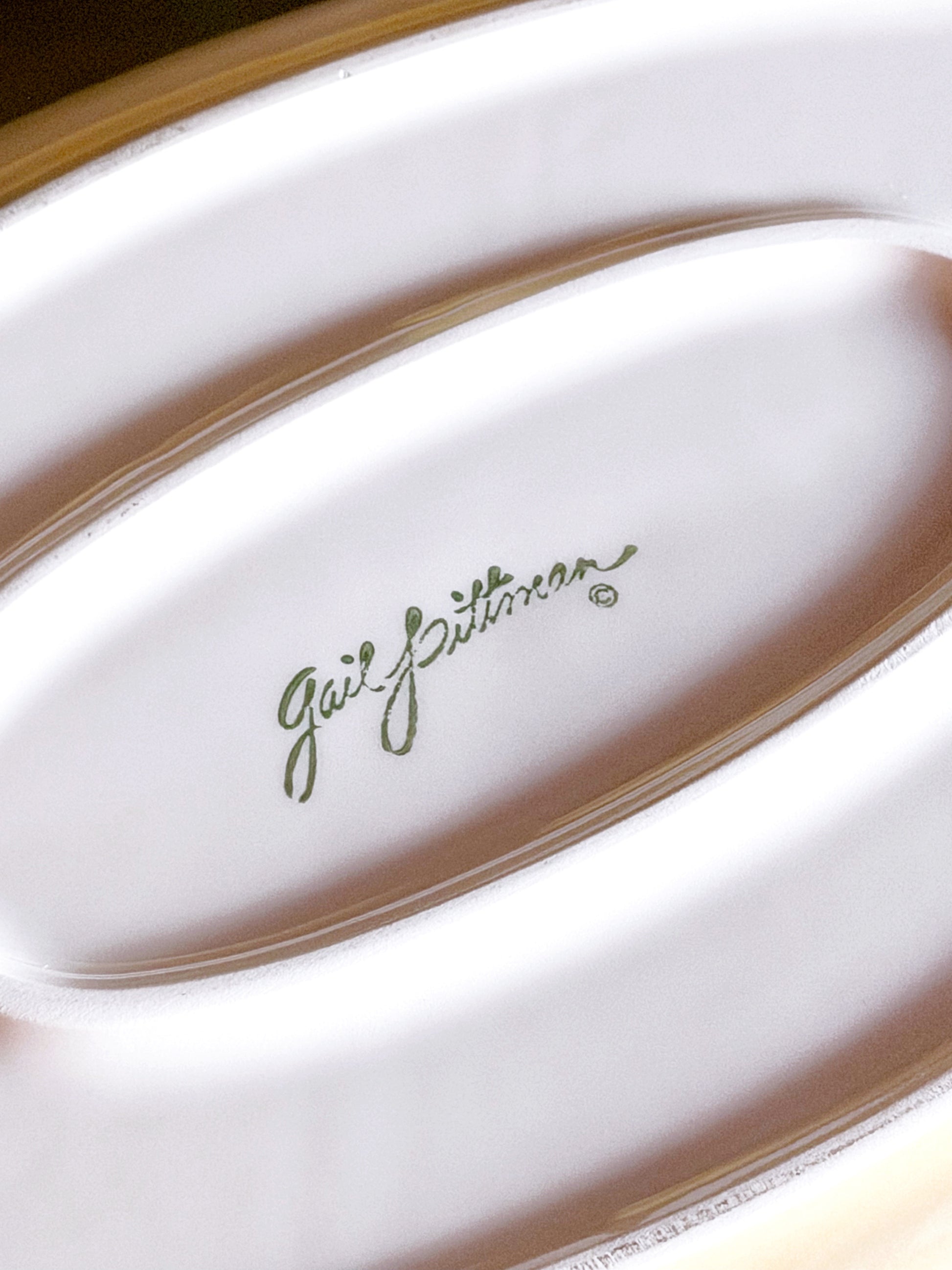 Close-up of a white ceramic dish with the brand name 'Gail Pittman' printed in green script in the center.