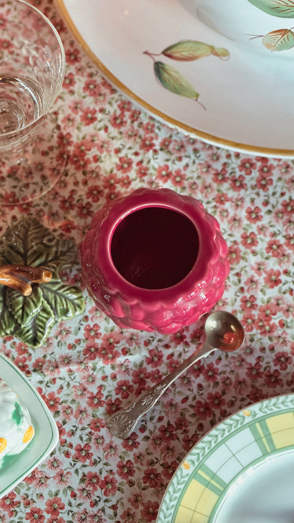 Vintage Ceramic Grape Jam Jar with Lid & Ladle on a floral tablecloth. Parts of patterned plates and a glass are visible around it.