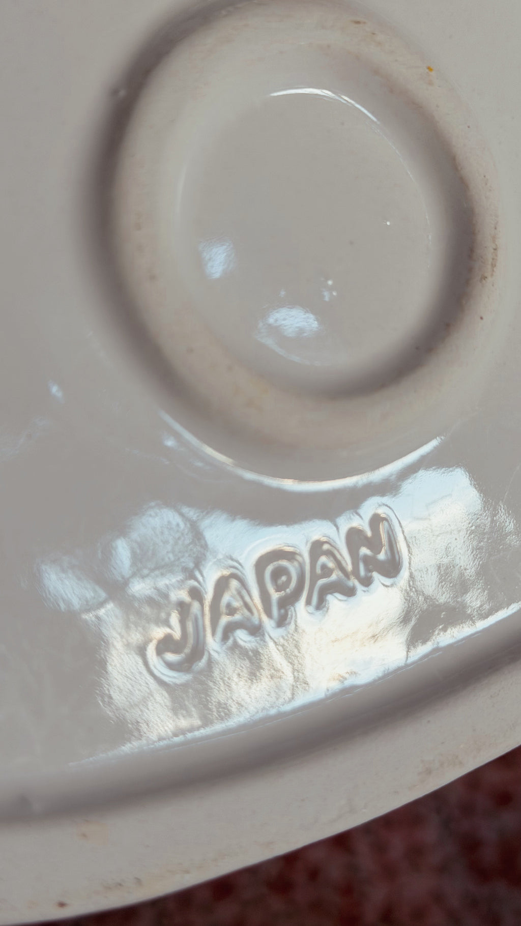 Close-up of the inside of a glossy off-white ceramic dish or plate, showing a circular indentation and an embossed 'JAPAN' mark near the bottom.
