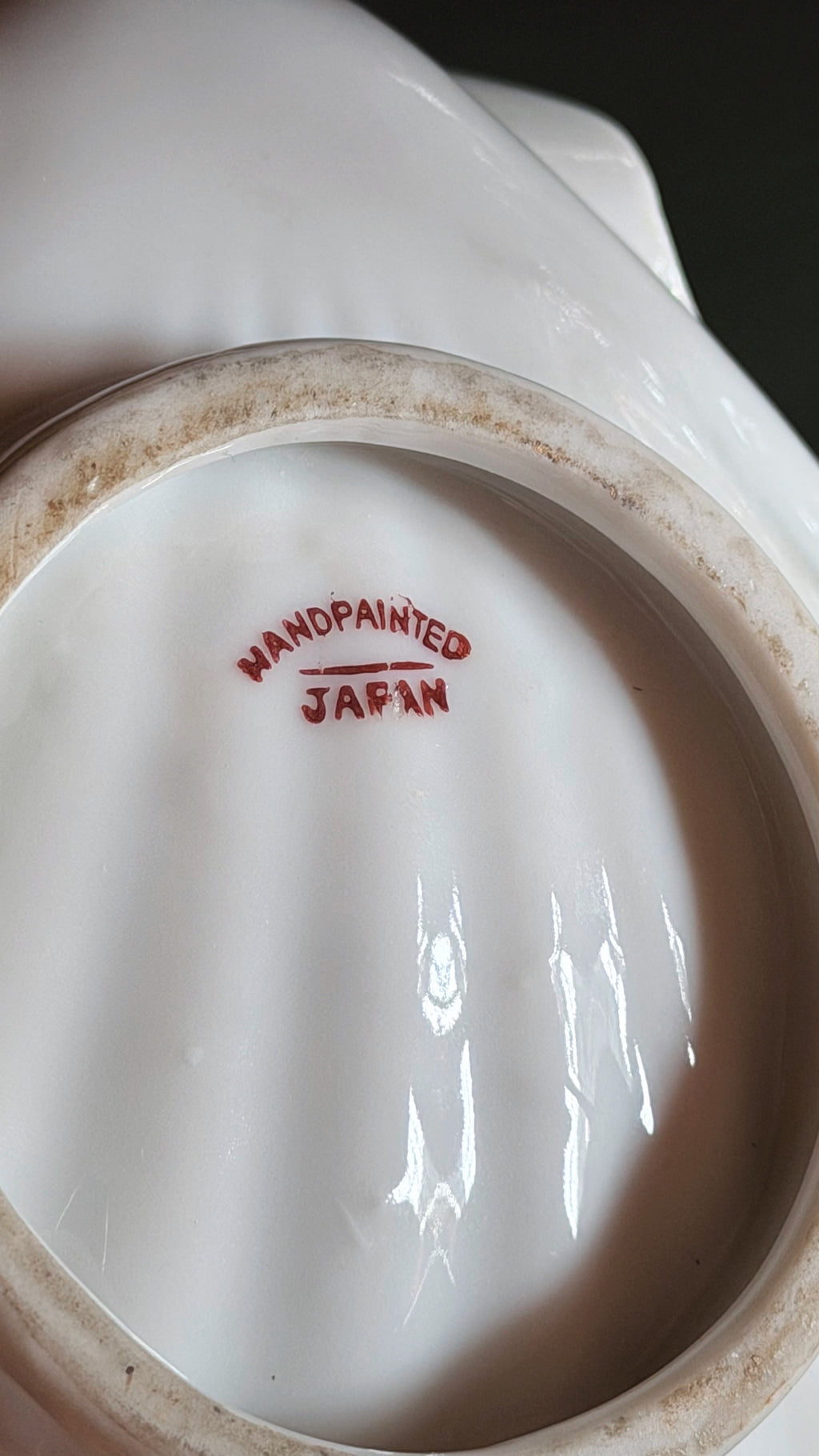 Close-up of the inside bottom of a white ceramic bowl or cup, showing a red stamp that reads 'HANDPAINTED JAPAN' on a dark background.