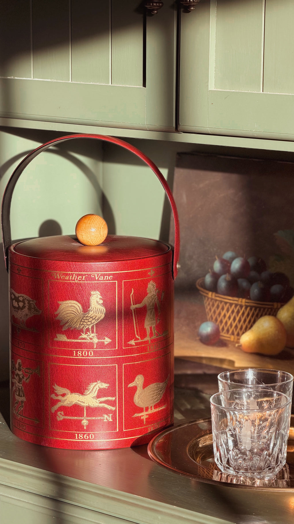 Vintage Georges Briard Weathervane Ice Bucket, placed on a kitchen counter beside two clear drinking glasses and a basket of fruit.