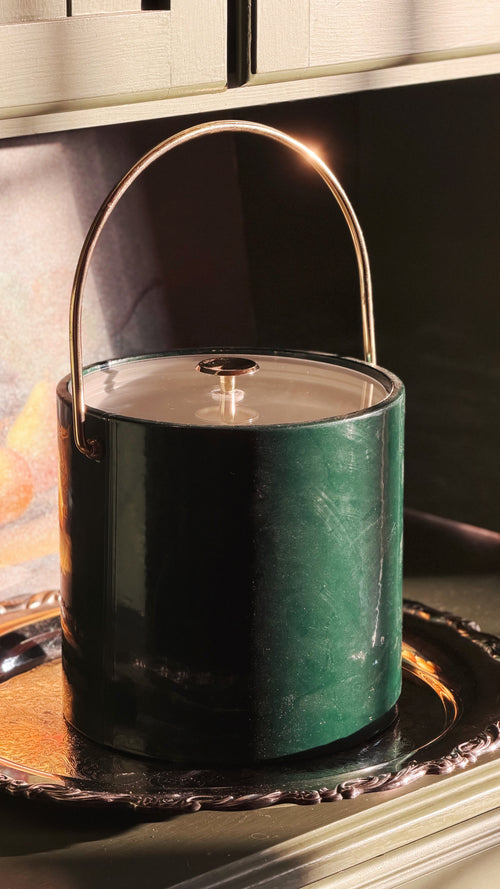 A Vintage Emerald Green Ice Bucket with Gold Handle & Lid, resting on an ornate silver tray.
