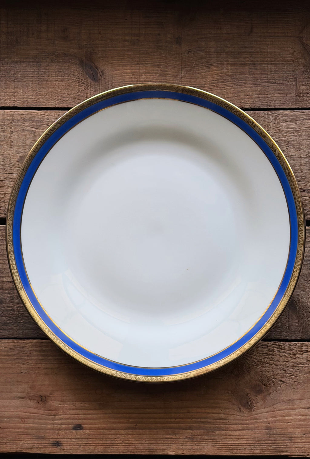 A Vintage Richard Ginori Palermo Blue Dinner Plate with a blue stripe and gold rim, photographed from directly above on a rustic dark wood background.