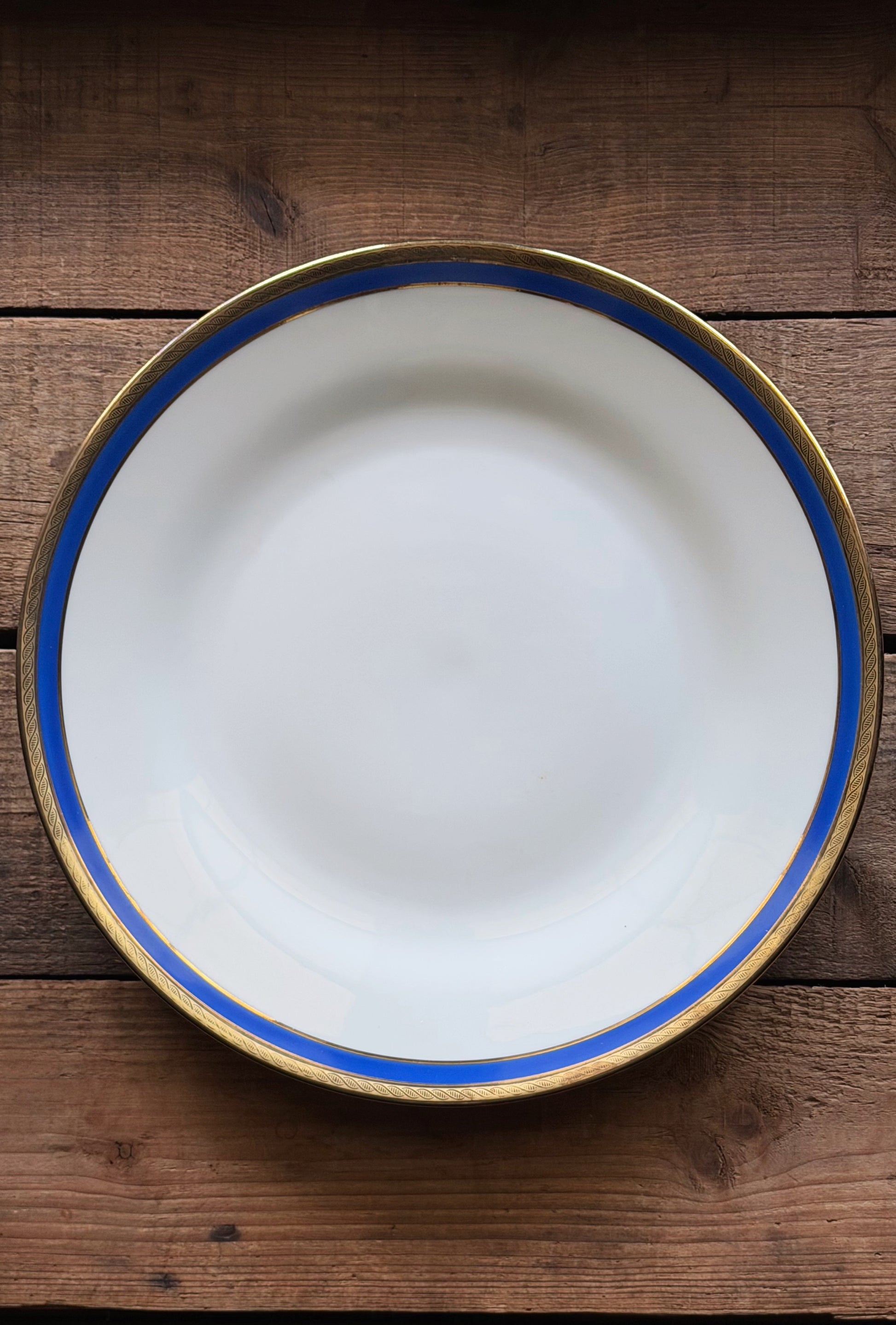 A Vintage Richard Ginori Palermo Blue Dinner Plate with a blue stripe and gold rim, photographed from directly above on a rustic dark wood background.