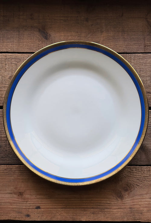 A Vintage Richard Ginori Palermo Blue Dinner Plate with a blue stripe and gold rim, photographed from directly above on a rustic dark wood background.