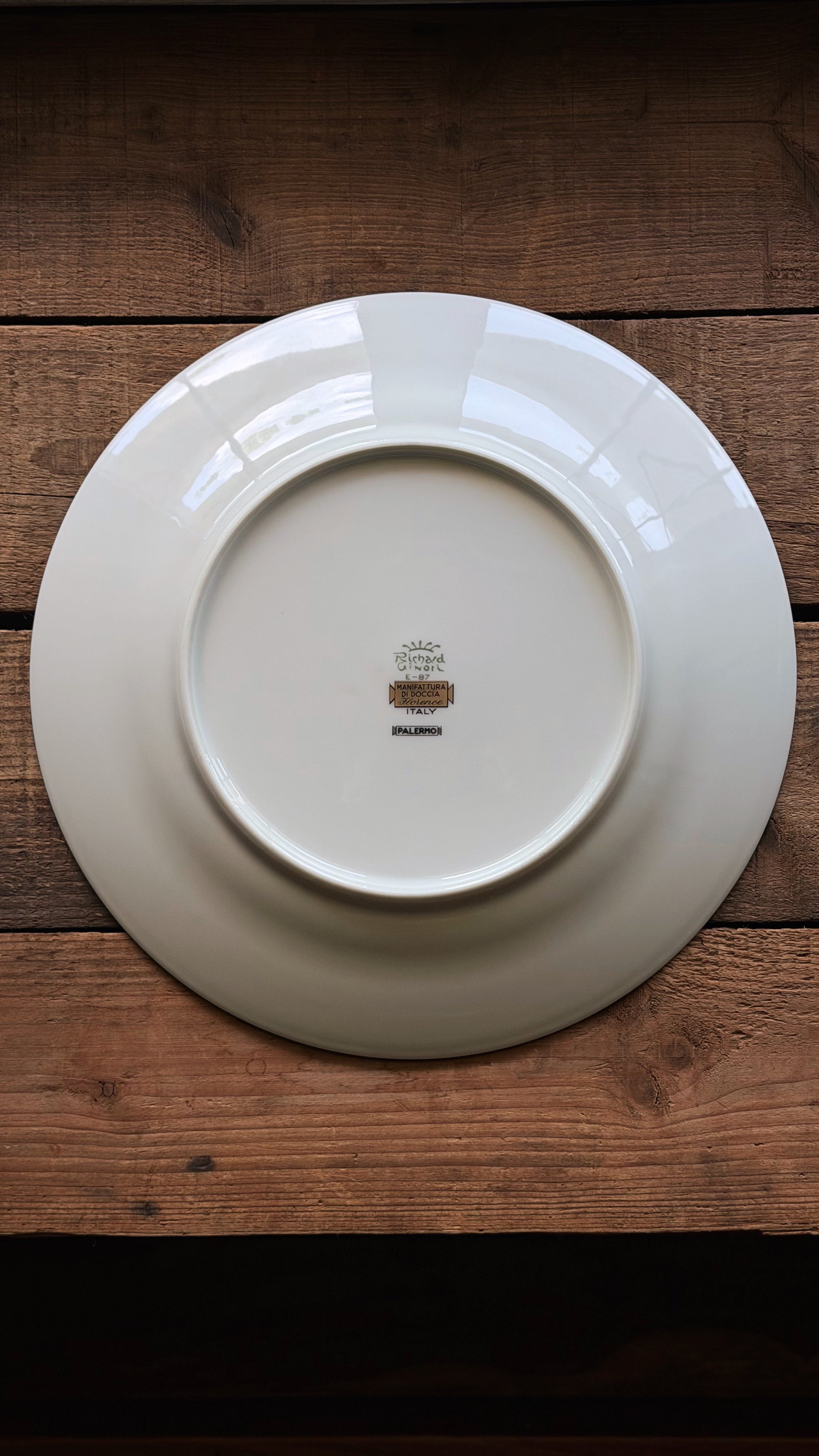 A Vintage Richard Ginori Palermo Blue Dinner Plate shown from the back, featuring a small central printed logo, placed on a rustic dark brown wooden surface.