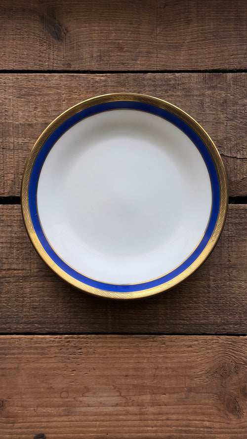 A title: Vintage Richard Ginori Palermo Blue Bread & Butter Plate with a wide blue band and a gold rim, photographed from directly above on a rustic dark wood plank surface.