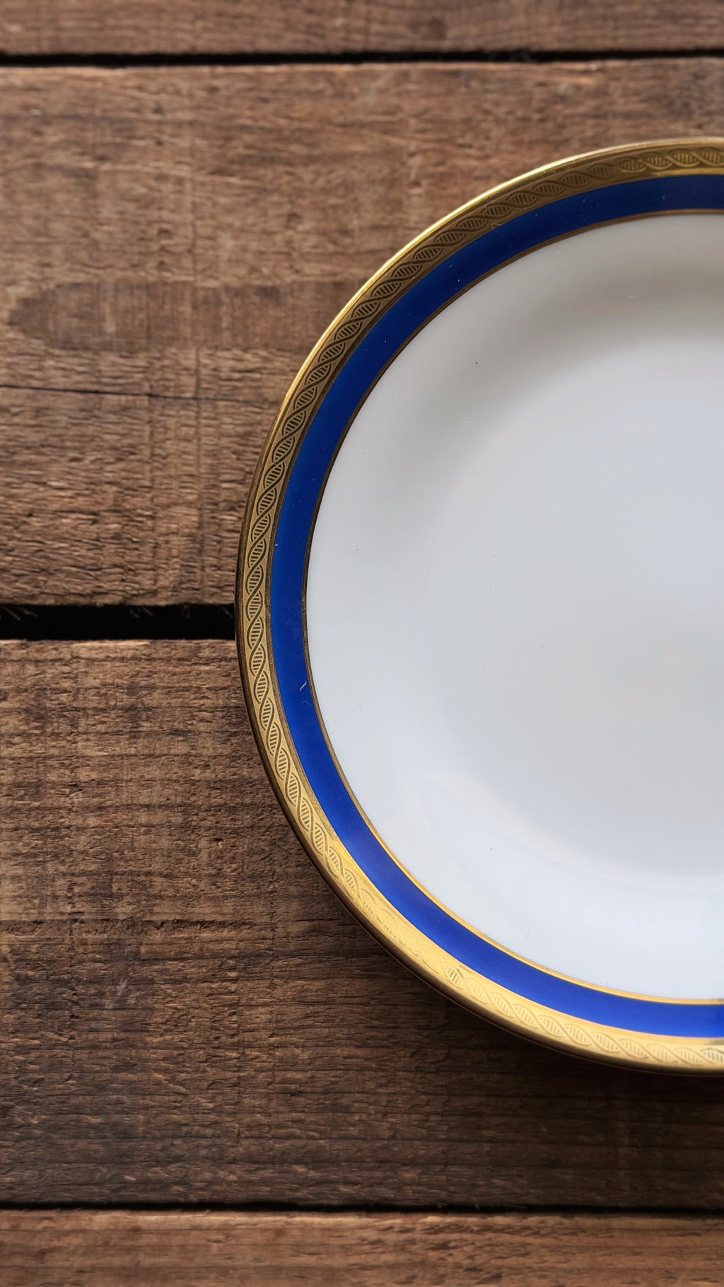 A close-up of a title: Vintage Richard Ginori Palermo Blue Bread & Butter Plate  with a blue and gold rim, placed on a rustic dark wood background.