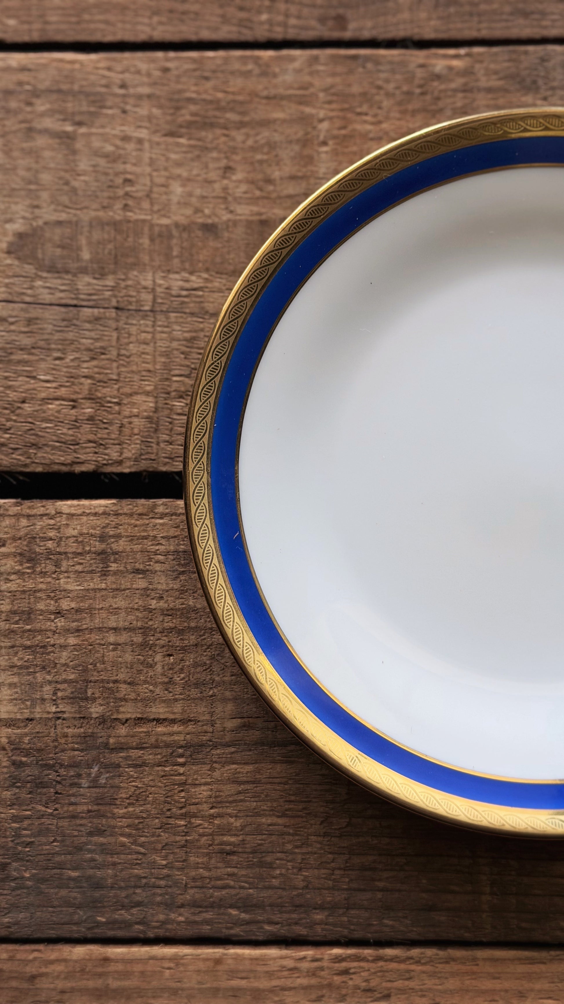 A close-up of a title: Vintage Richard Ginori Palermo Blue Bread & Butter Plate  with a blue and gold rim, placed on a rustic dark wood background.