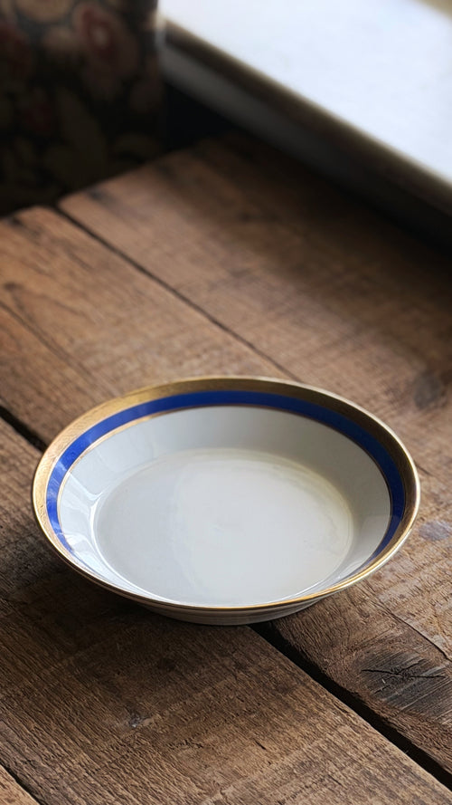 A Vintage Richard Ginori Palermo Blue Fruit Bowl with a blue and gold rim, resting on a rustic wooden tabletop.