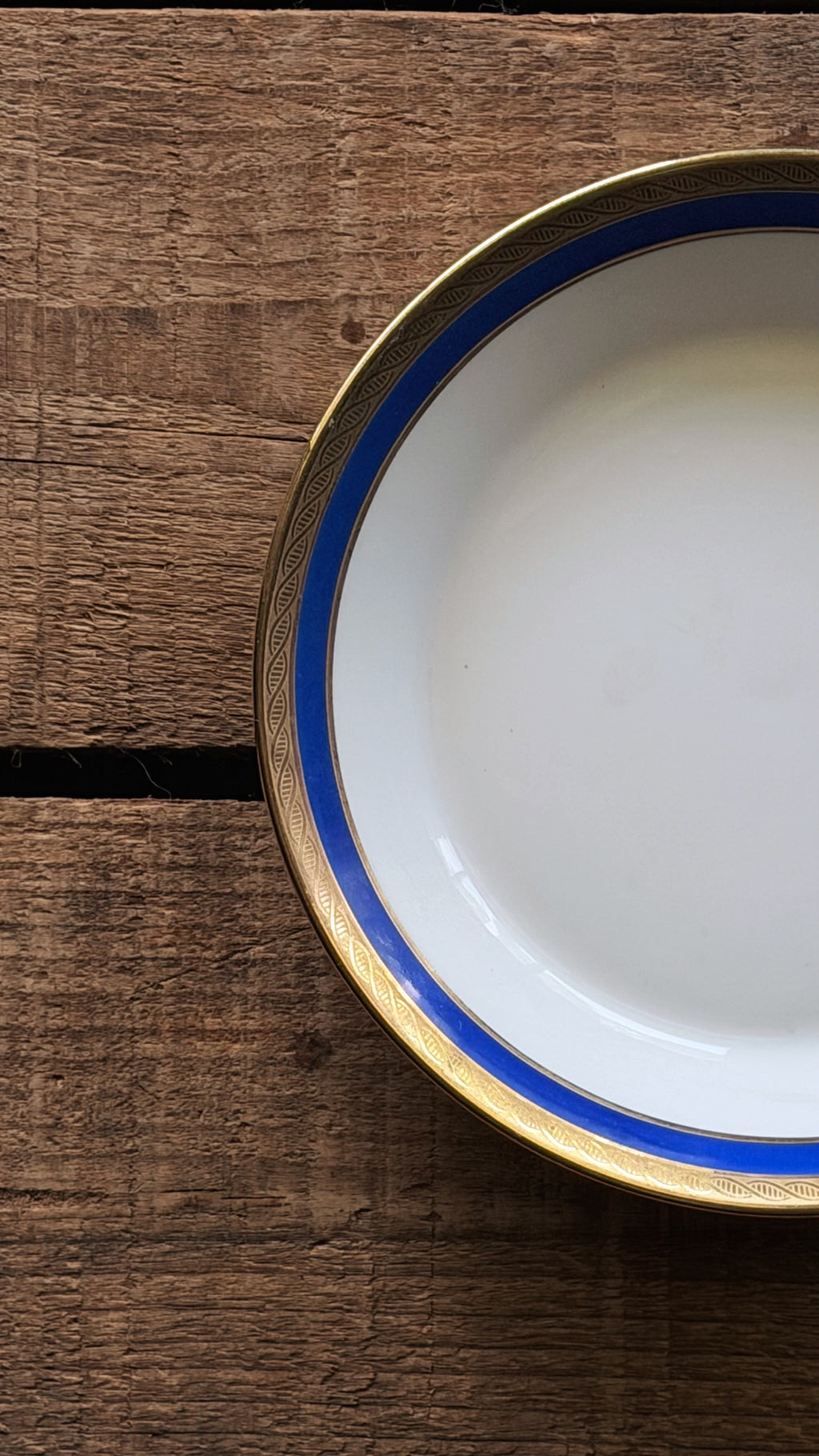 A close-up top-down view of a Vintage Richard Ginori Palermo Blue Fruit Bowl with a blue and gold rim, placed on a rustic dark brown wooden surface.