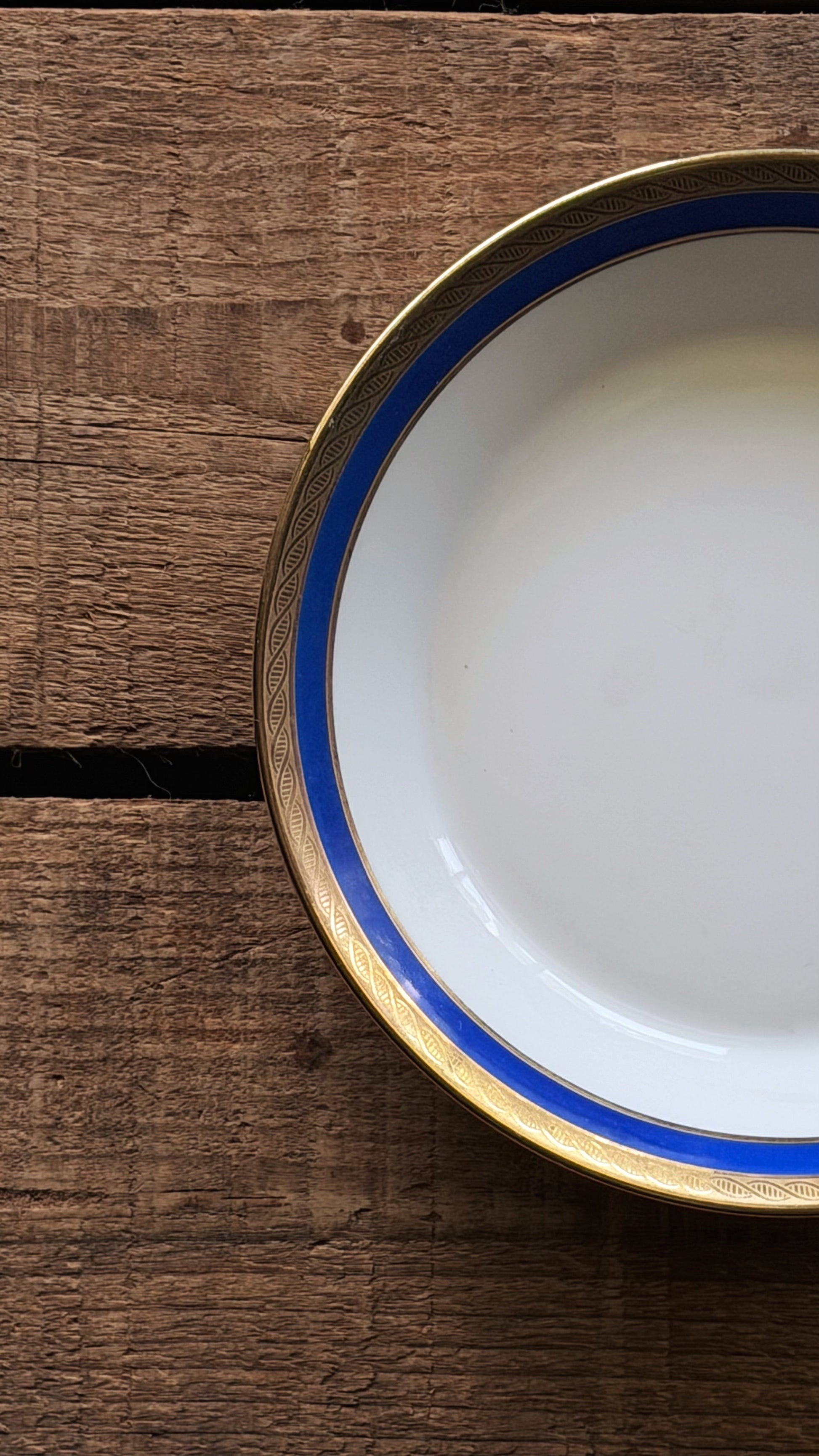 A close-up top-down view of a Vintage Richard Ginori Palermo Blue Fruit Bowl with a blue and gold rim, placed on a rustic dark brown wooden surface.