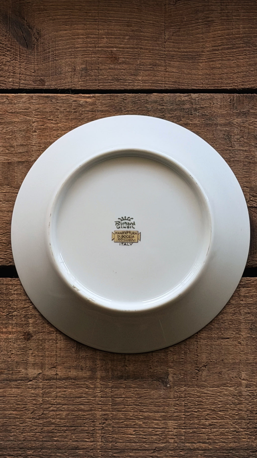 A Vintage Richard Ginori Palermo Blue Fruit Bowl shown from the back, featuring a small gold and black 'Ginori' mark in the center, placed on a rustic dark brown wooden surface.