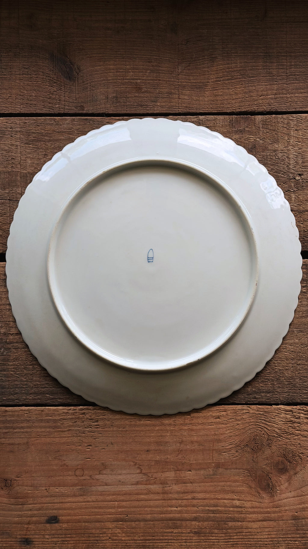 Underside of a Vintage Royal Vienna Hand Painted Salad Plate with a scalloped rim, photographed from directly above on a rustic dark brown wooden surface.