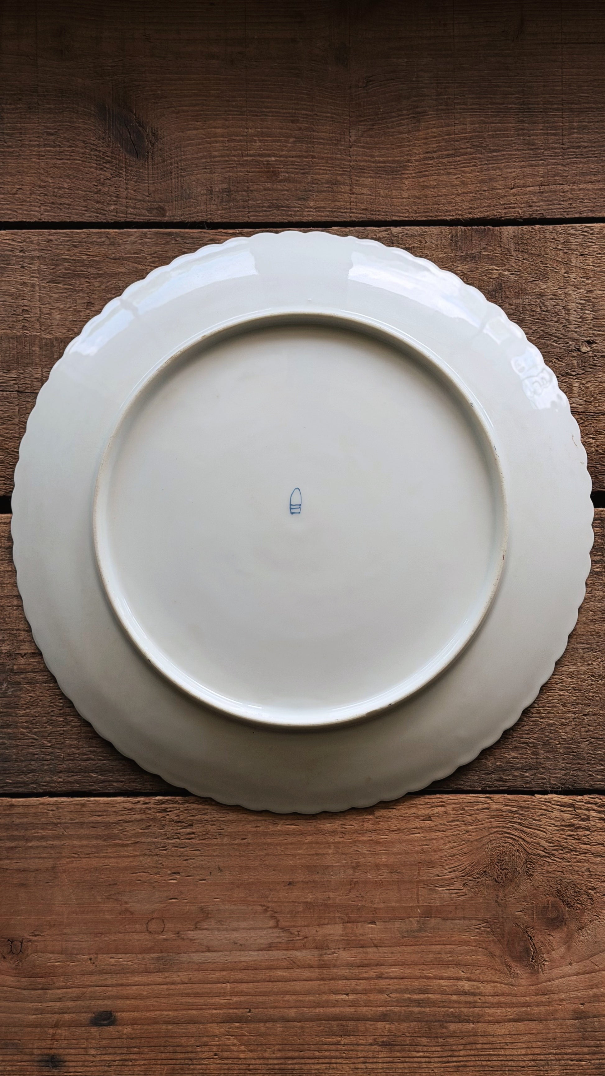 Underside of a Vintage Royal Vienna Hand Painted Salad Plate with a scalloped rim, photographed from directly above on a rustic dark brown wooden surface.