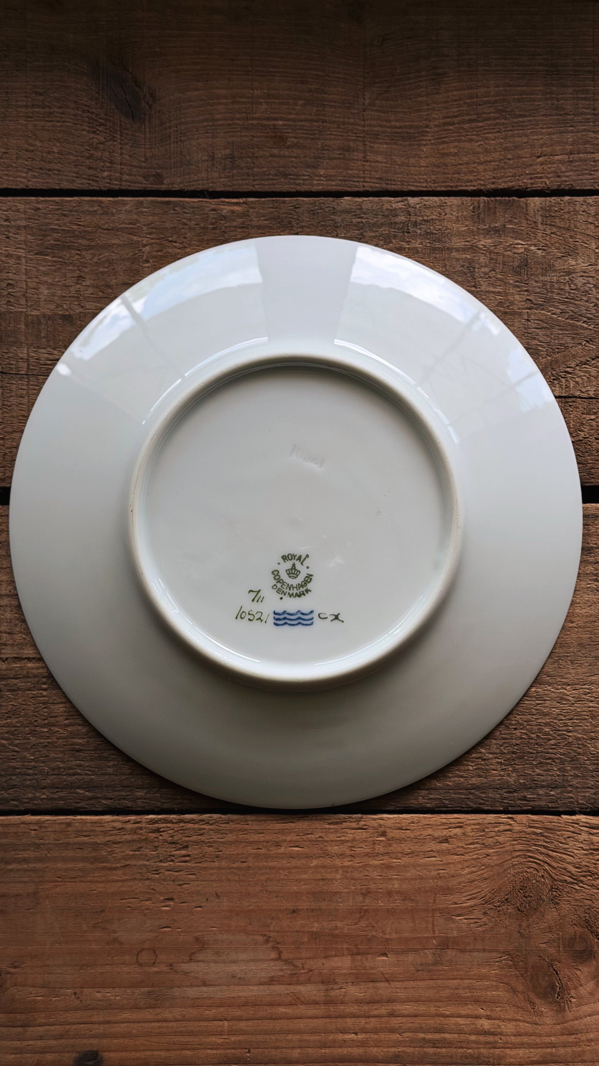 A Vintage Royal Copenhagen Brown Iris Salad Plate shown from the back, featuring a small blue and green printed mark near the center, placed on a dark brown wooden surface.