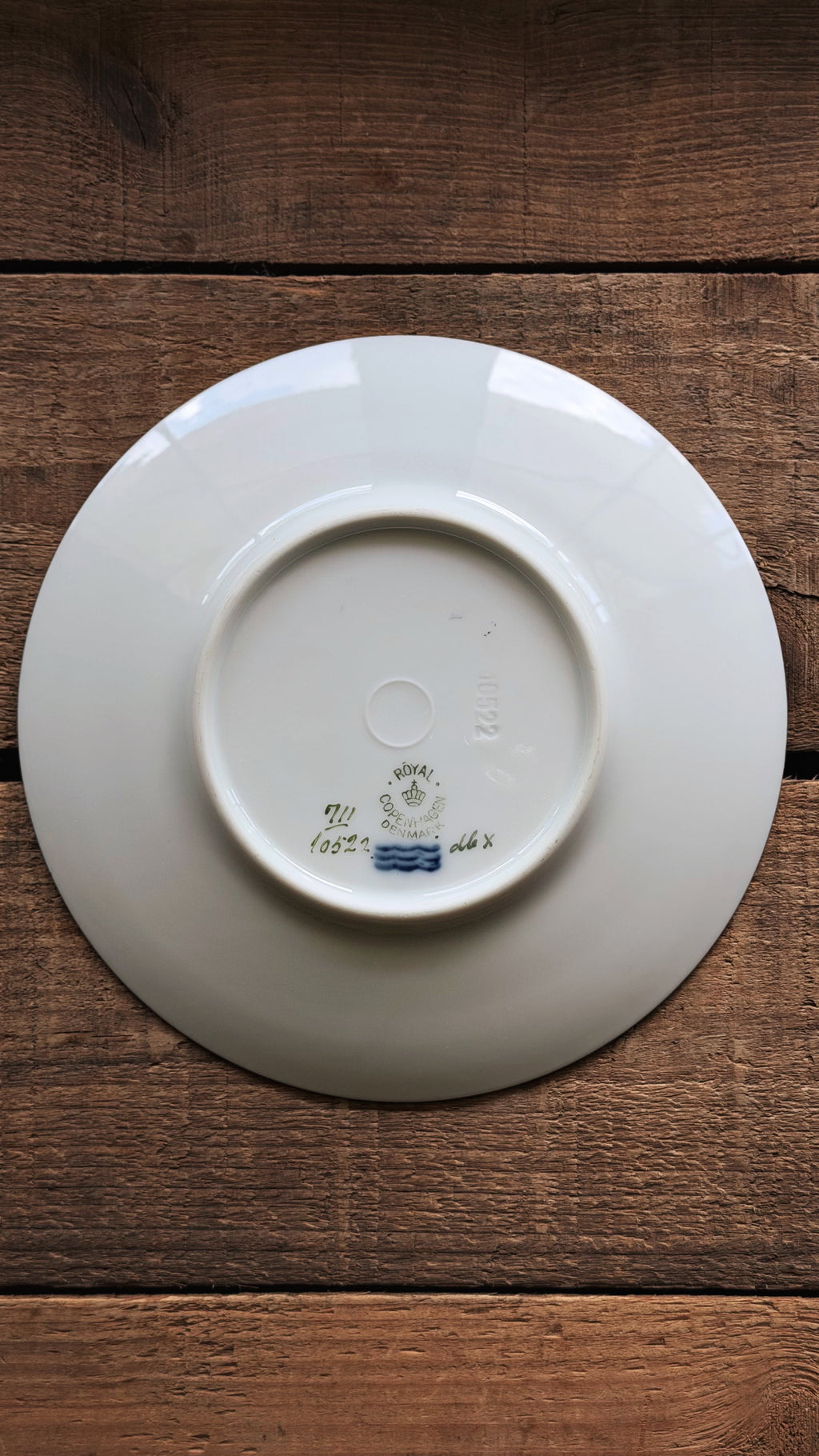 The underside of a Vintage Royal Copenhagen Brown Iris Bread and Butter Plate with printed maker's marks, photographed from above on a dark brown wooden surface.