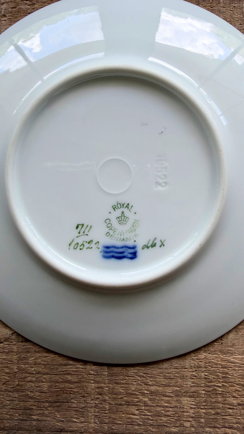 The underside of a white porcelain plate  resting on a brown wooden surface, showing Royal Crown of England maker's marks and a blue stripe.