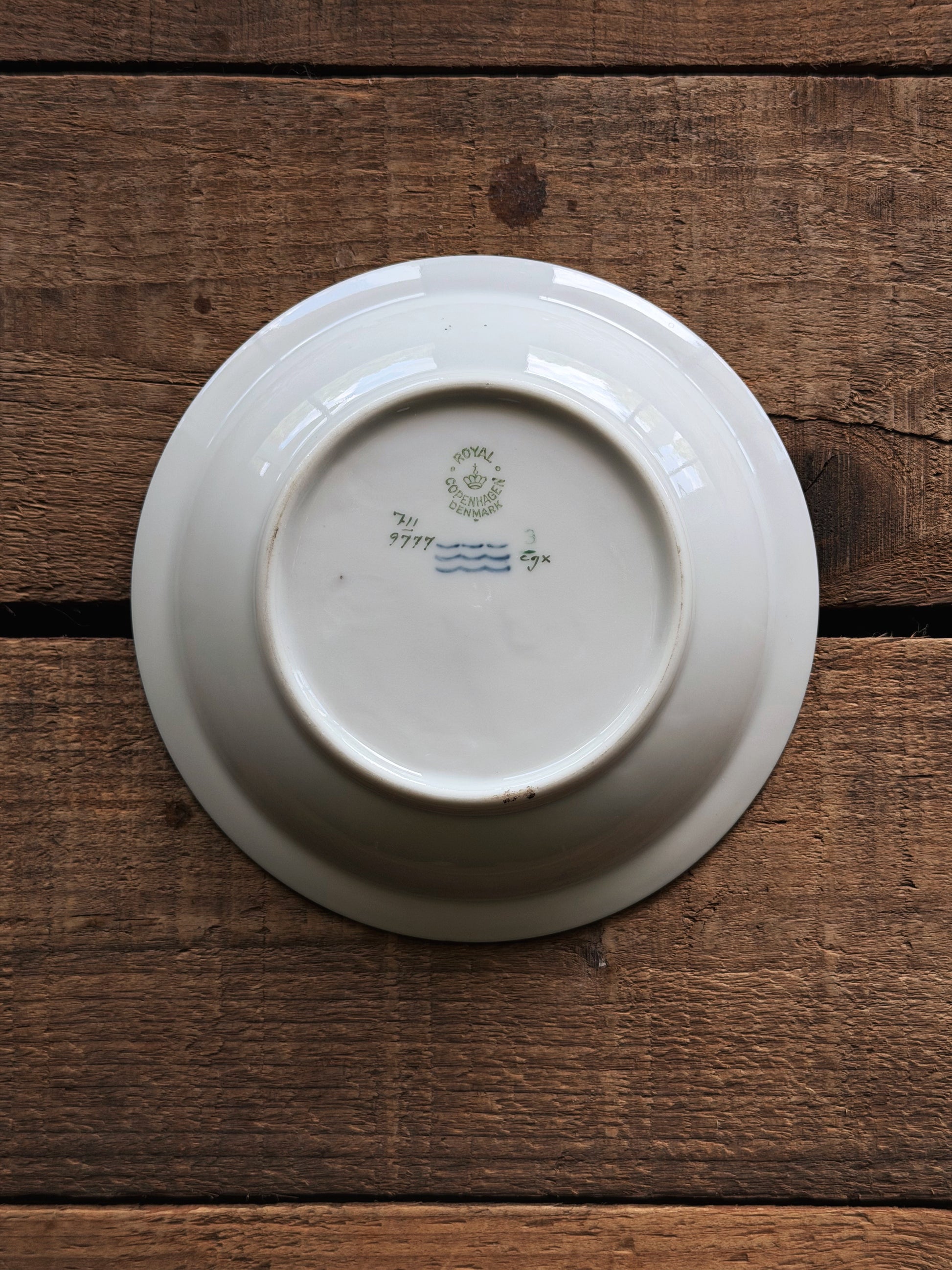 The bottom of a Vintage Royal Copenhagen Brown Iris Fruit Bowl with a hand-painted green and blue mark, photographed from directly above on a rustic wooden plank background.