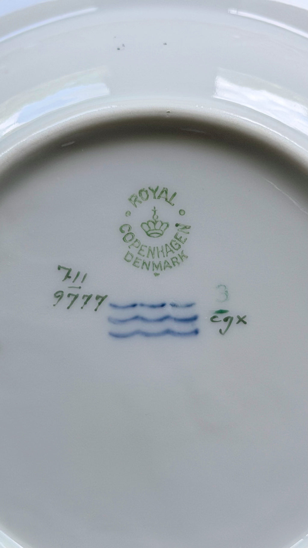 Close-up of the inside bottom of a white porcelain plate showing green and blue Royal Copenhagen Denmark markings.
