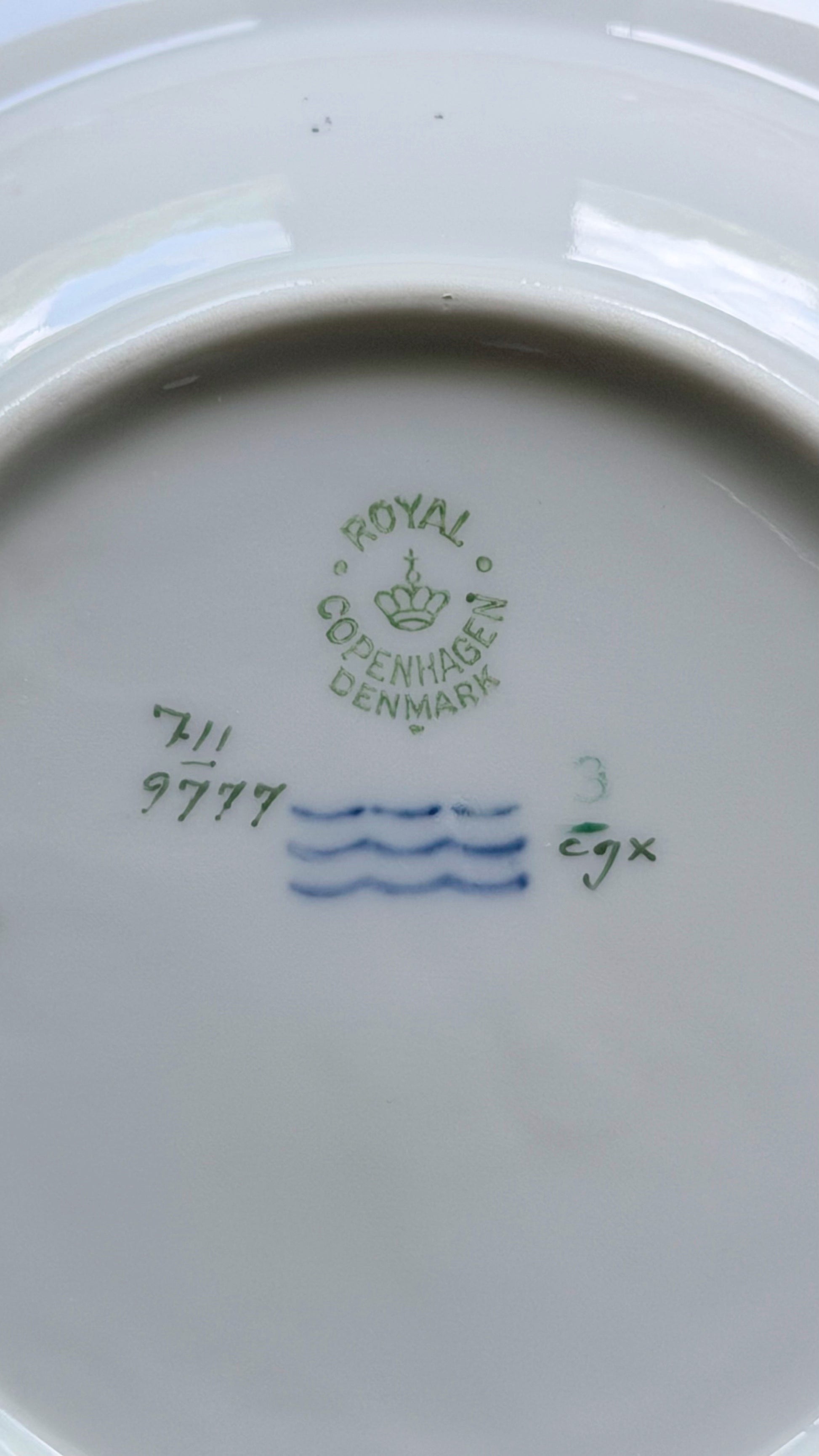 Close-up of the inside bottom of a white porcelain plate showing green and blue Royal Copenhagen Denmark markings.