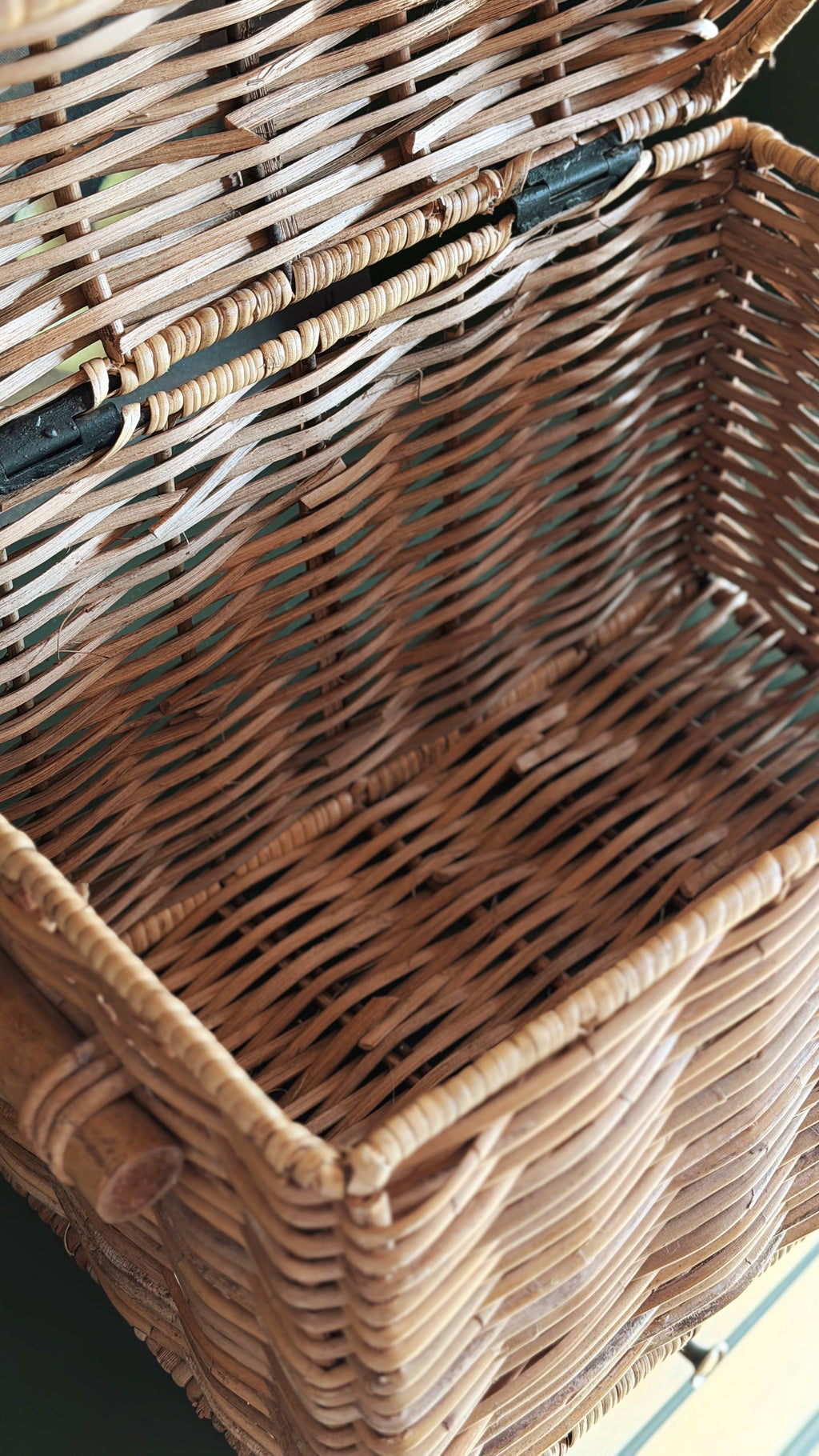 Close-up of a natural woven wicker basket with a hinged lid, showing the detailed texture of the interlaced rattan in warm tan and brown tones.