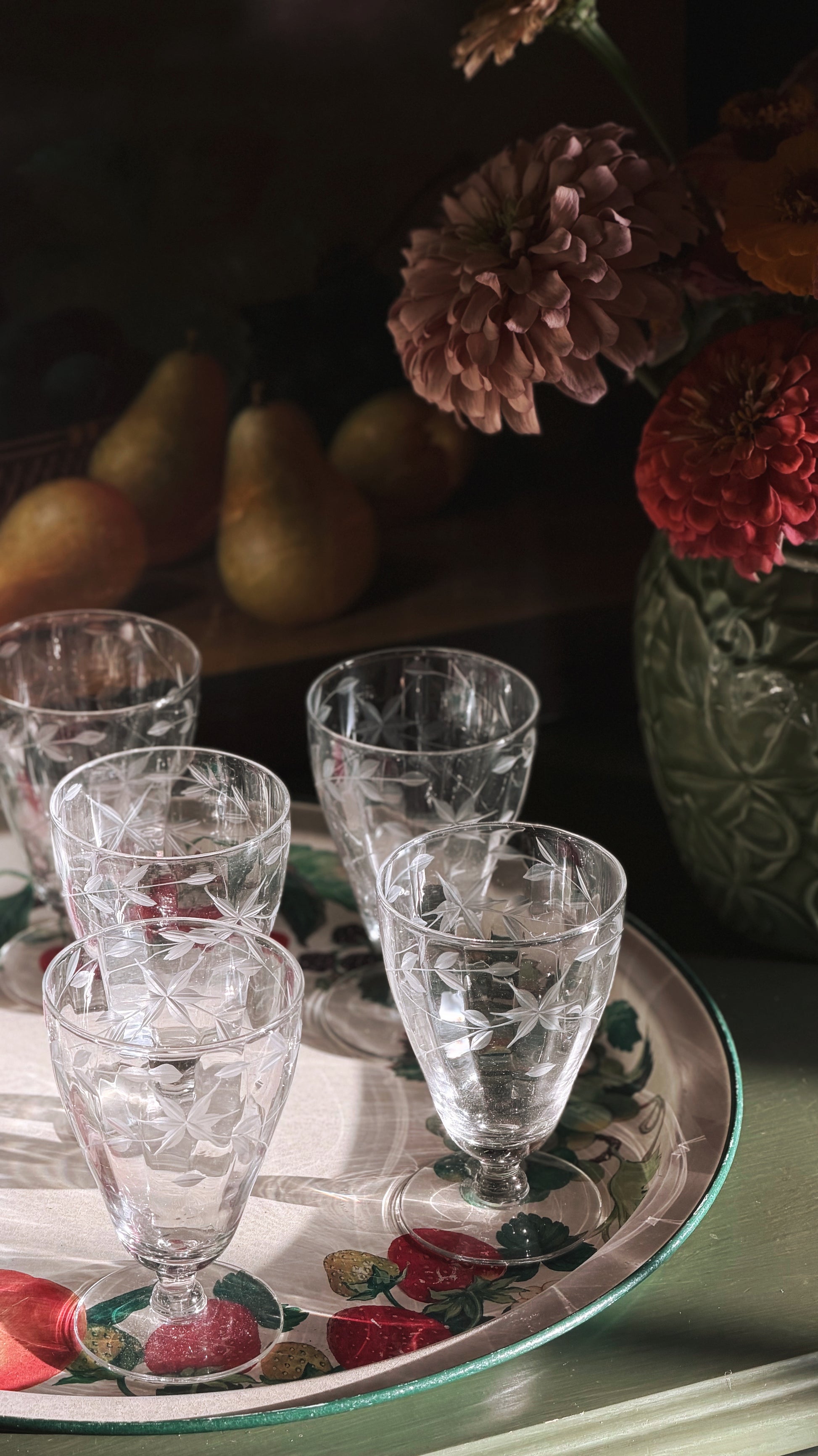 Vintage Etched Crystal Starburst Aperitif | Cordial Glasses arranged on a decorative floral tray, with a dark rustic background featuring pears and flowers.