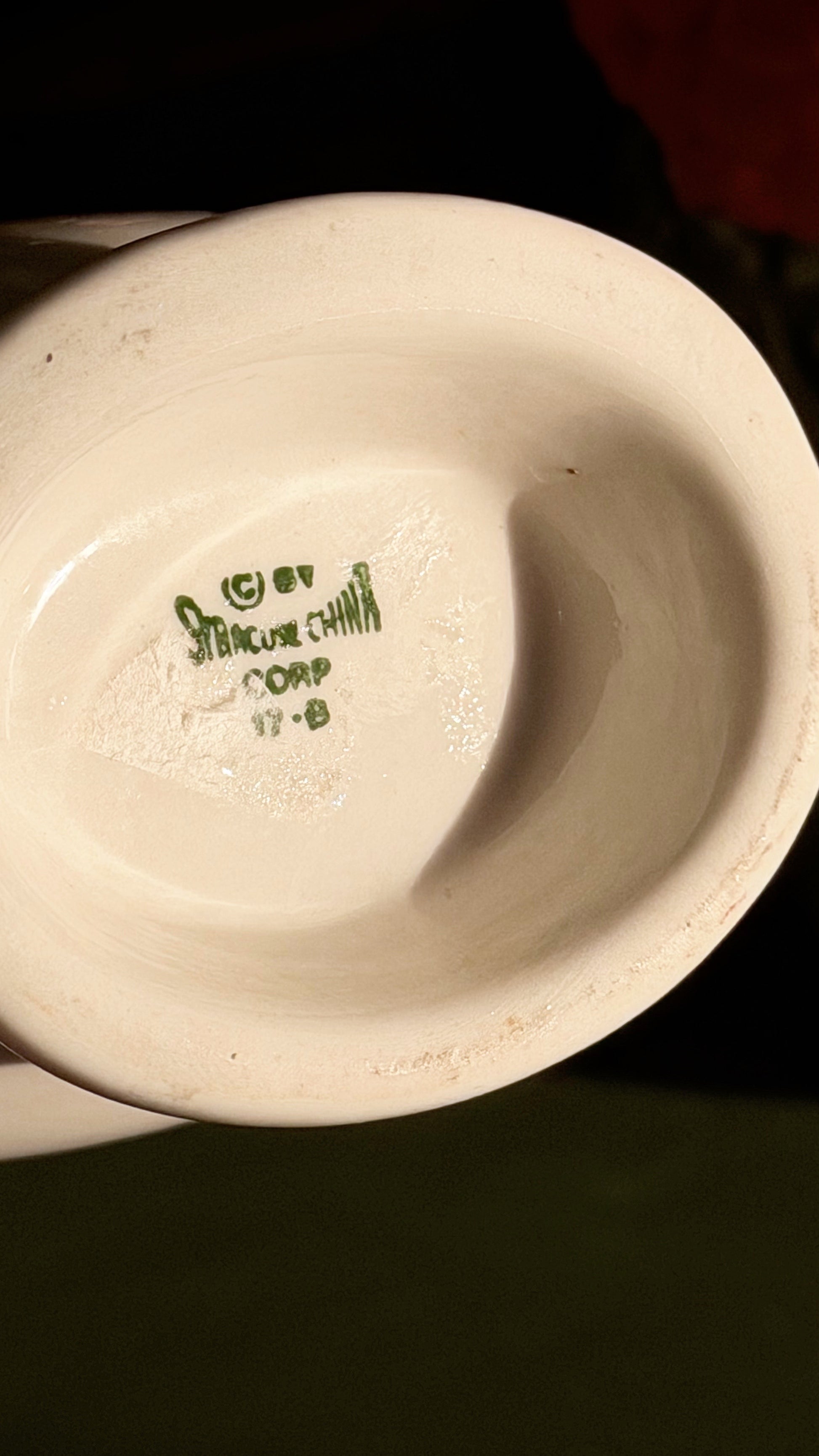 Close-up of the underside bottom of a white gravy boat, showing a green Syracuse China mark on a dark background.