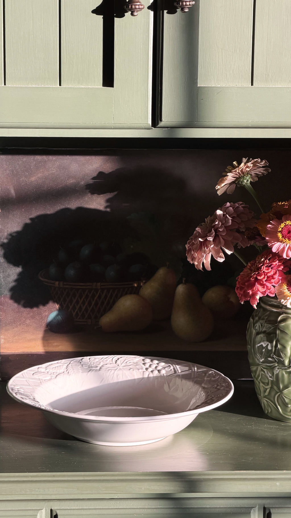 A Mikasa English Countryside bowl with a delicate embossed floral pattern around the rim, set on a dark tabletop in a styled kitchen scene with flowers and pears in the background.