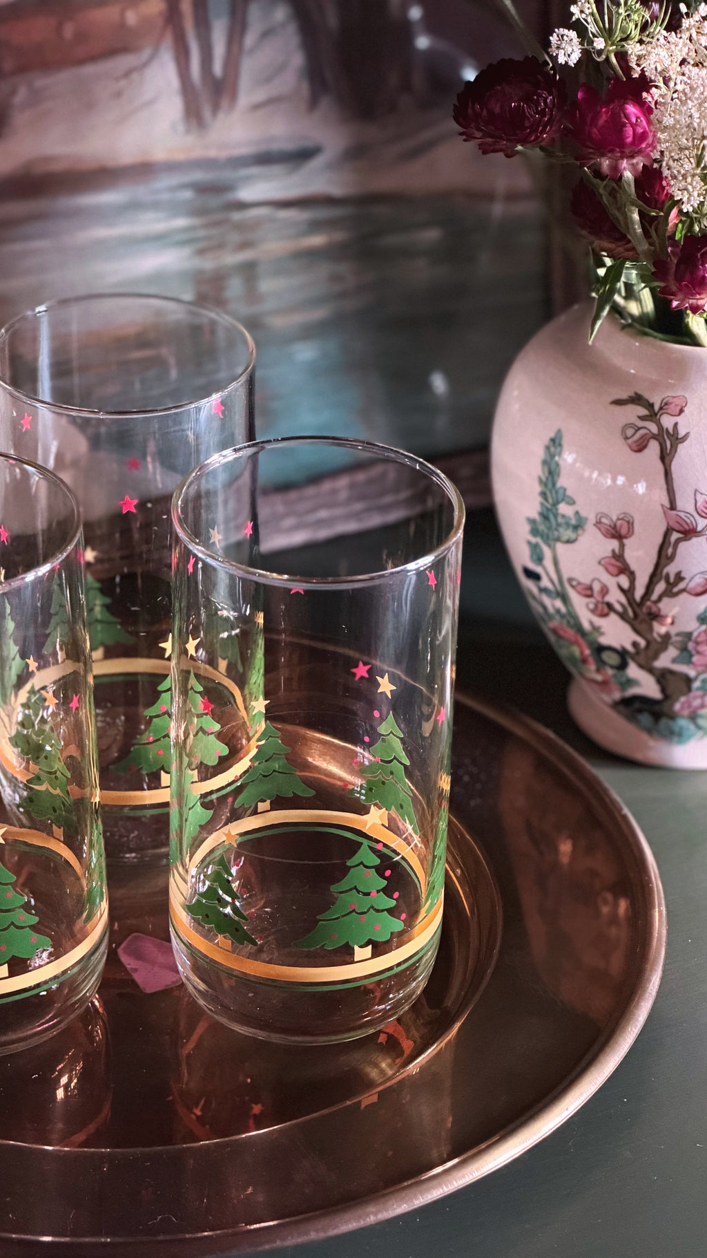 Vintage Christmas Tree Gold Band Glass Tumblers with green Christmas tree and gold rim designs, arranged on a round copper tray next to a pink floral vase.