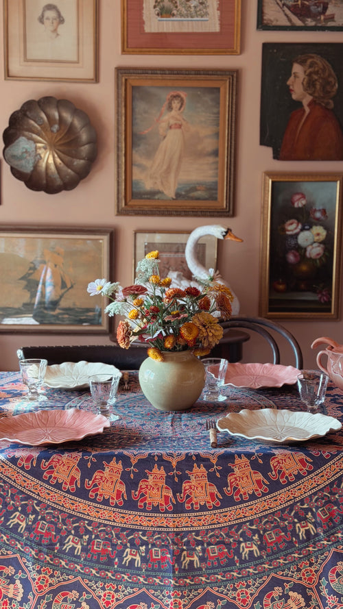 A Vintage Indian Cotton Floral Block Print Tablecloth, pink plates, and a central vase of autumn flowers, set against a warm wall covered in framed vintage portraits and prints.