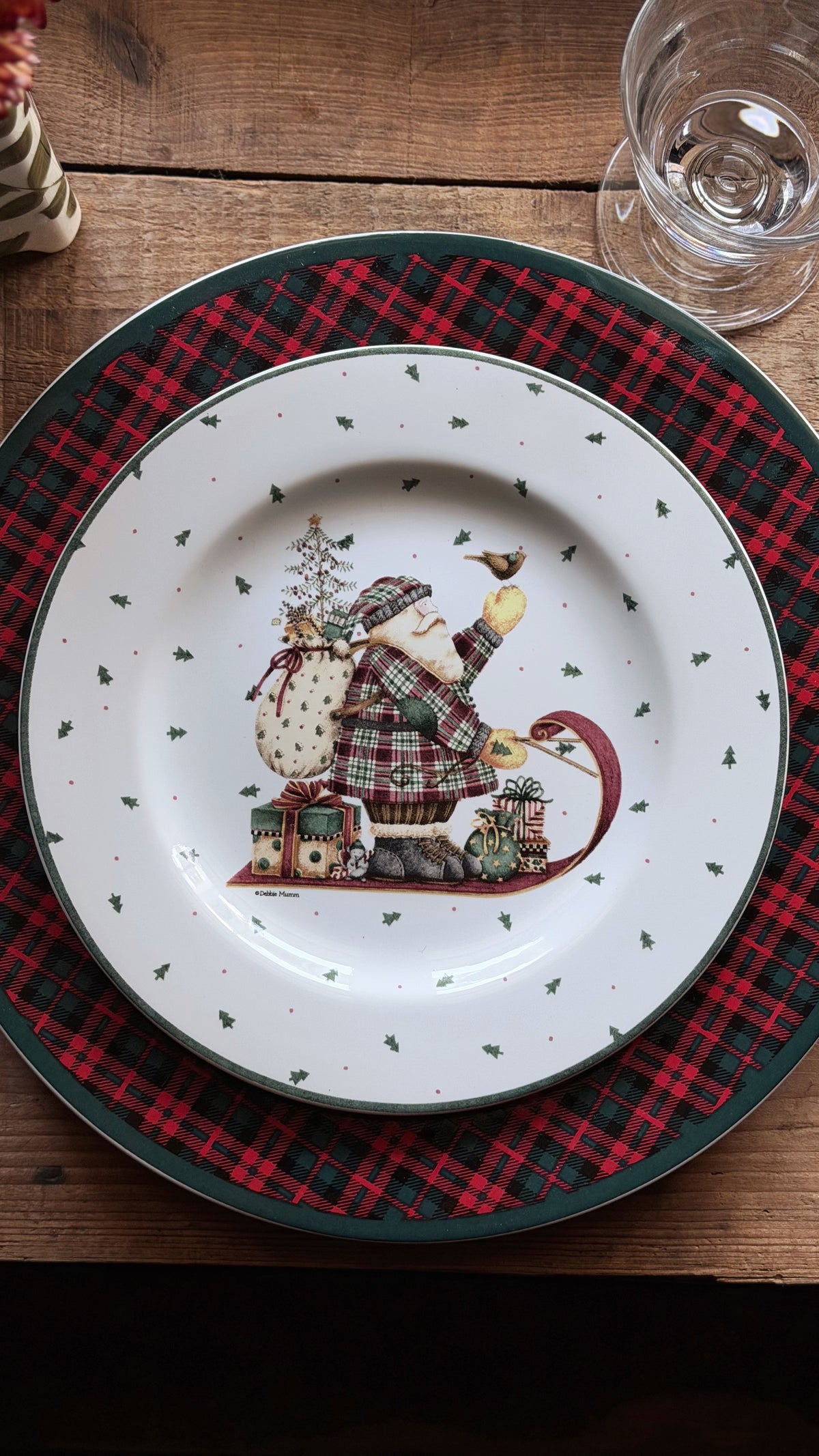 A festive Christmas dinner plate featuring a Santa Claus in a sleigh illustration, styled on a red and black plaid charger plate over a wooden table.
