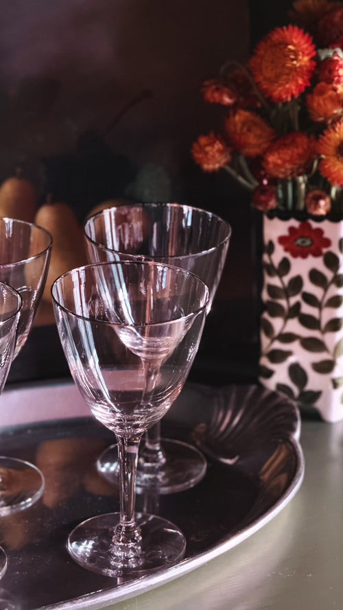 Clear crystal wine glasses arranged on a silver tray, with a dark background and a vase of orange flowers in the rear.
